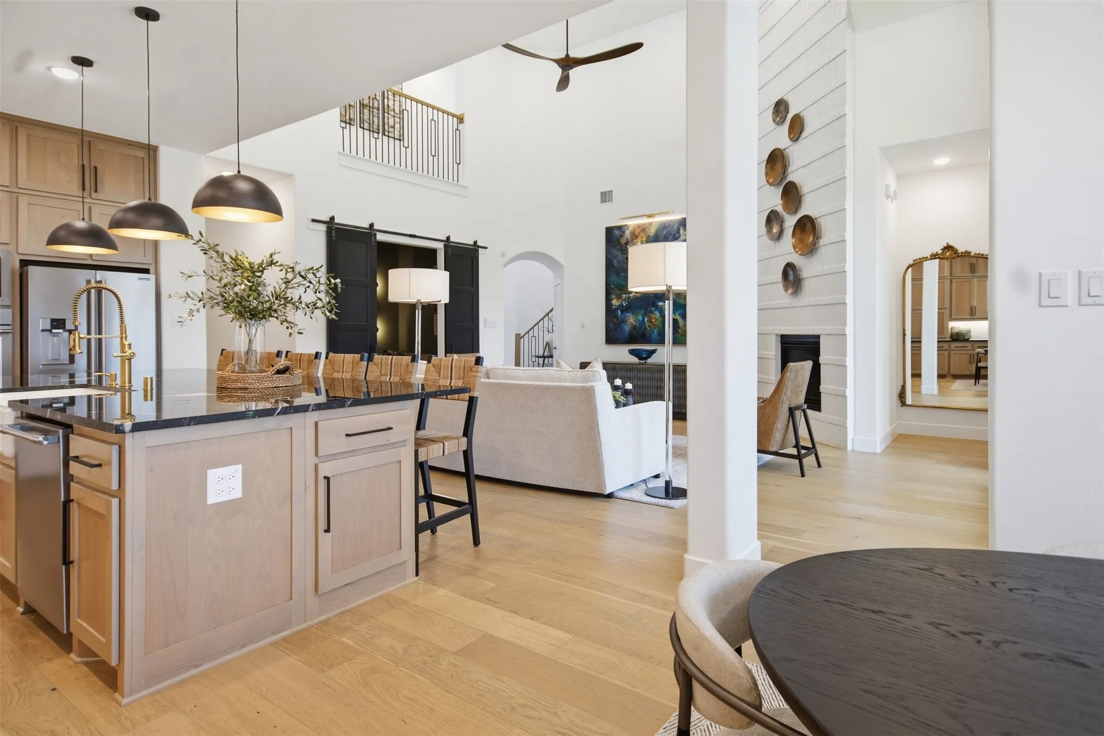 Open-concept living space with light wood-finish flooring, a kitchen island featuring a dark stone countertop, and a living area with a fireplace and vaulted ceilings