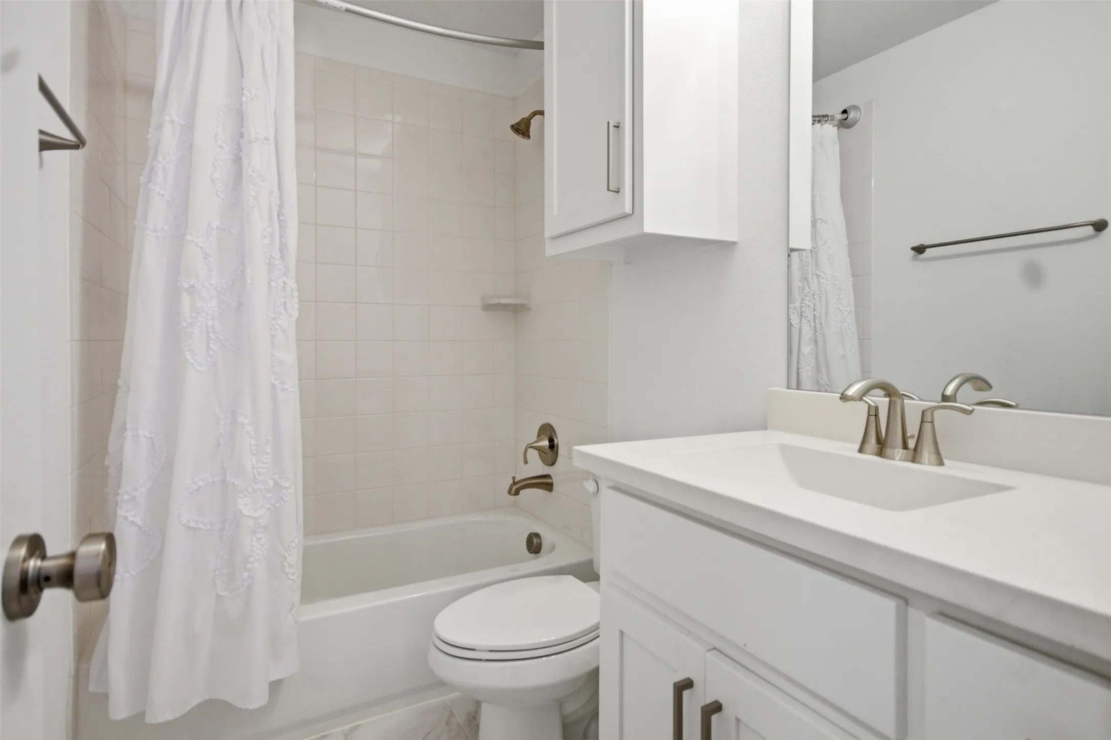 Bathroom featuring a bathtub with tile surround, a single vanity with an integrated sink, a large wall-mounted mirror, and a wall-mounted storage cabinet