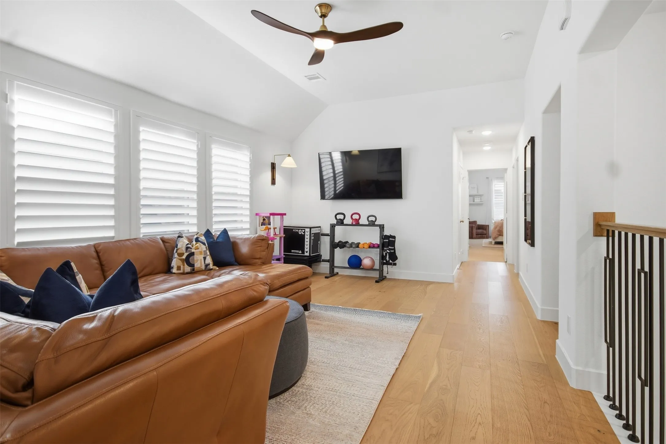 Spacious upper-level area featuring wood-finish flooring, a contemporary ceiling fan, and multiple windows with plantation shutters