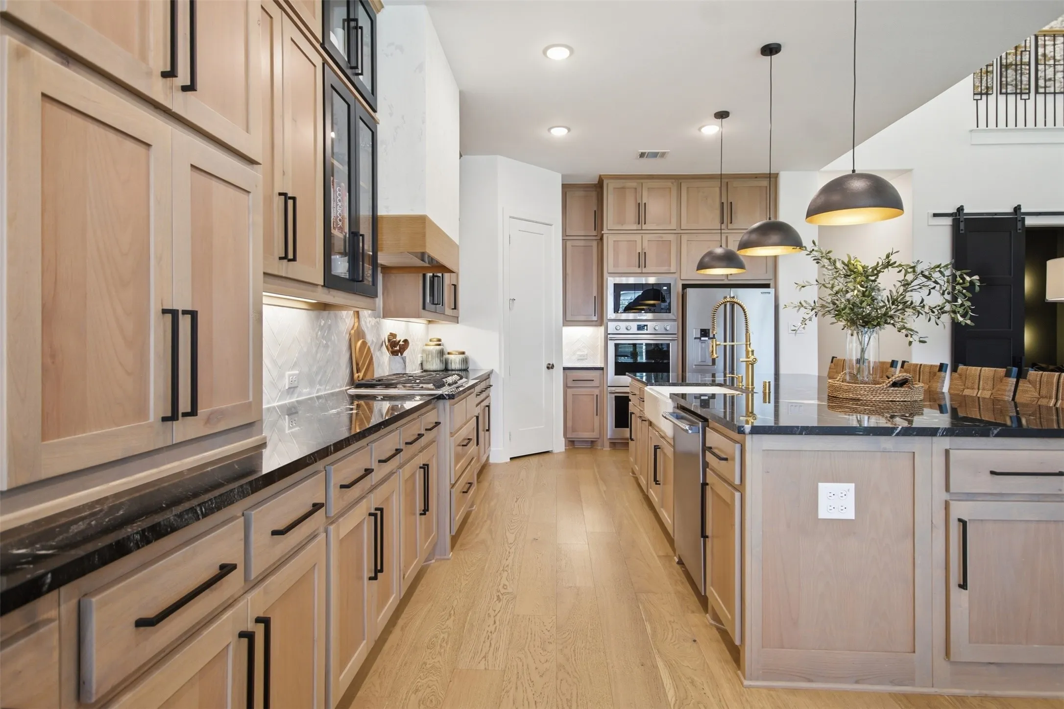 Gourmet kitchen featuring light wood-finish cabinetry, dark countertops, a large center island with pendant lighting, stainless steel appliances, and wood-finish flooring