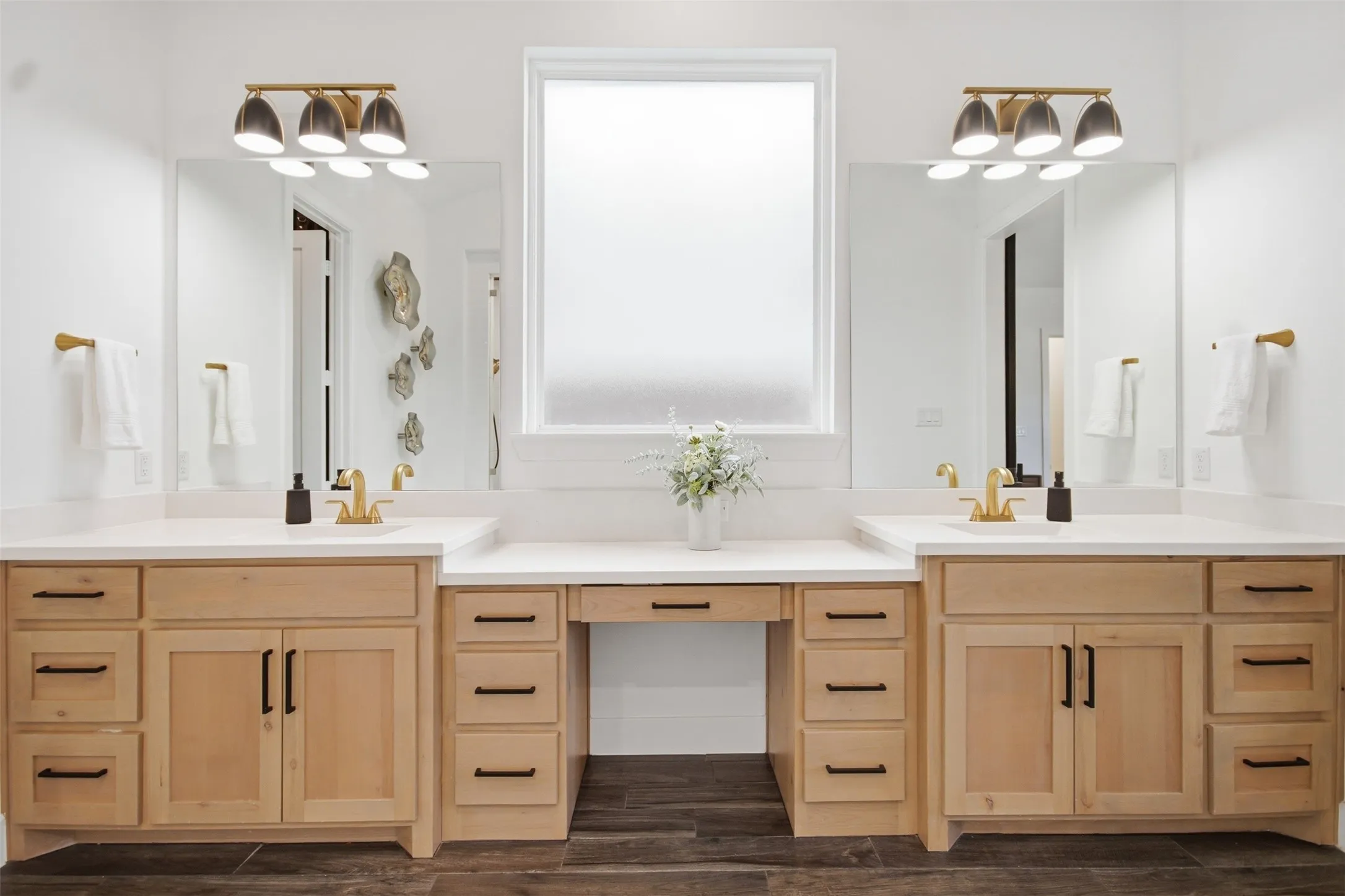 Dual vanities featuring light wood-finish cabinetry, white countertops, and gold-tone fixtures