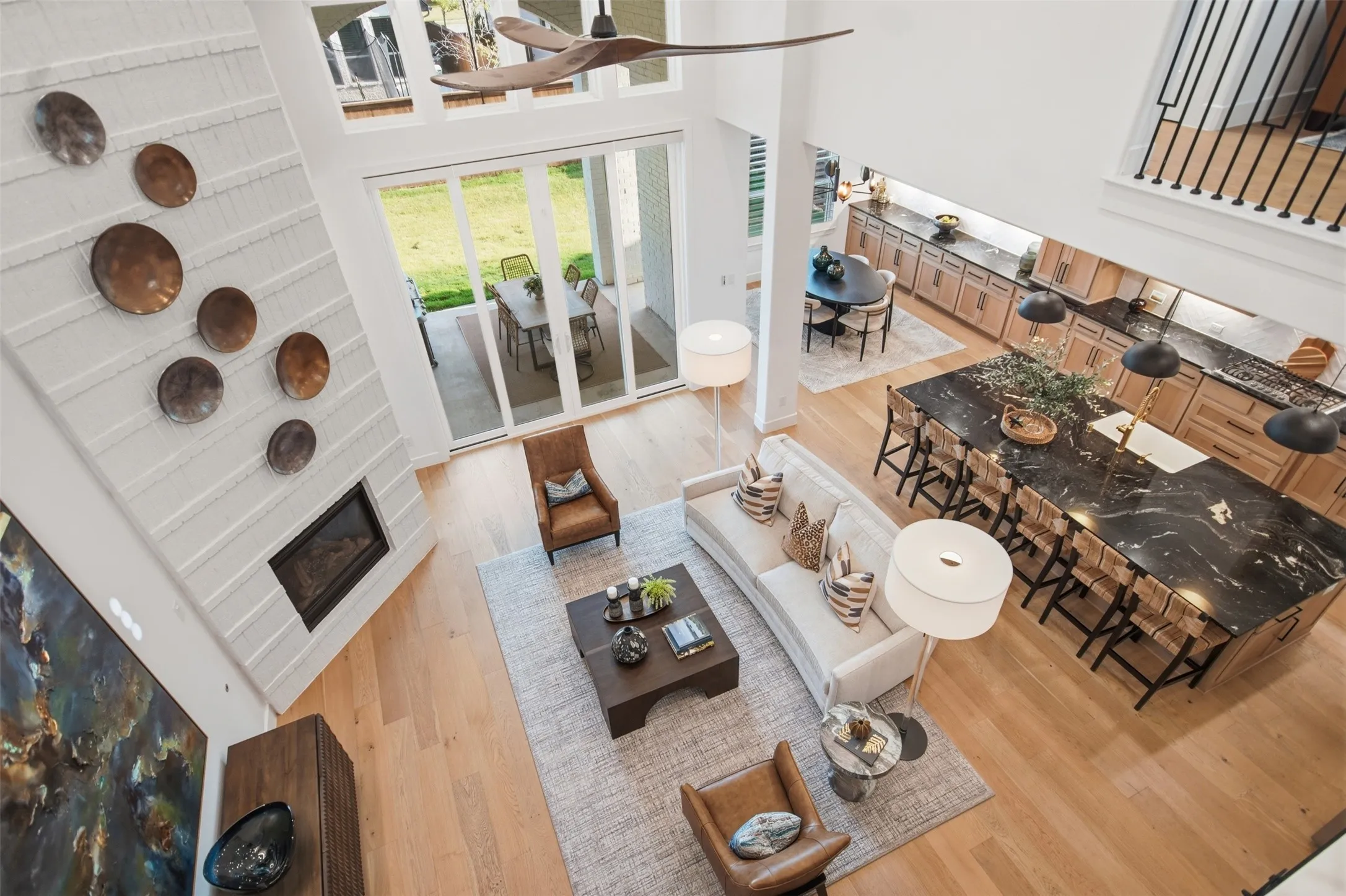 Two-story living area with wood-finish flooring, a contemporary fireplace with a textured surround, and expansive sliding glass doors opening to an outdoor patio