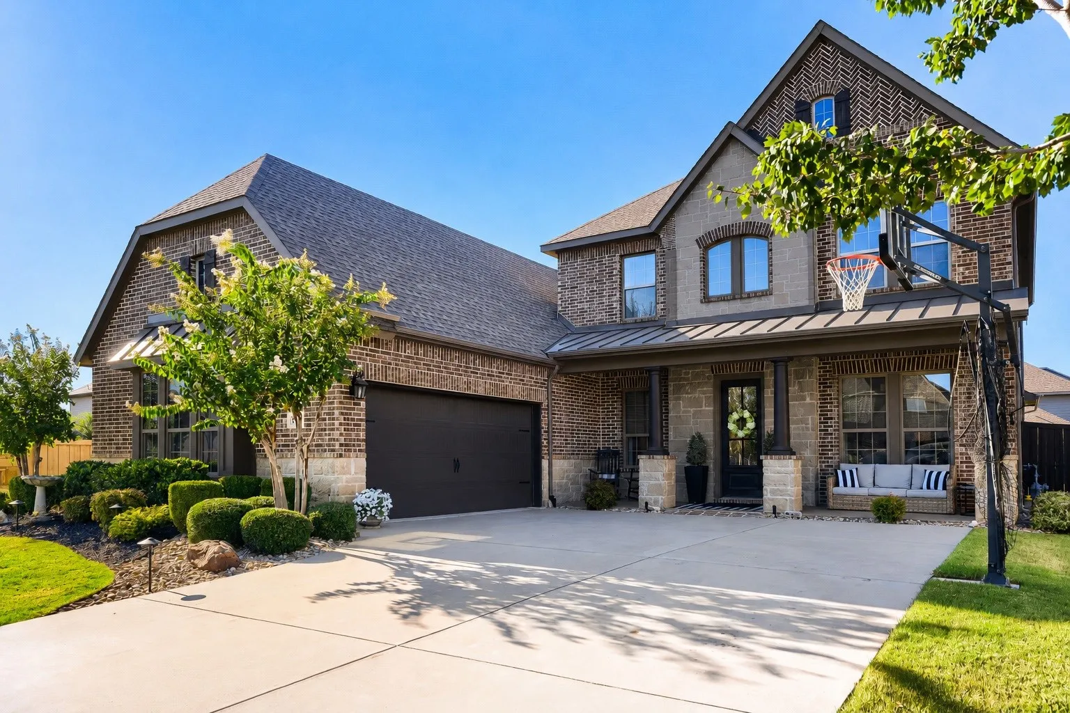 Brick and stone facade residence featuring a covered front porch, an attached two-car garage, multiple windows, and a landscaped front yard