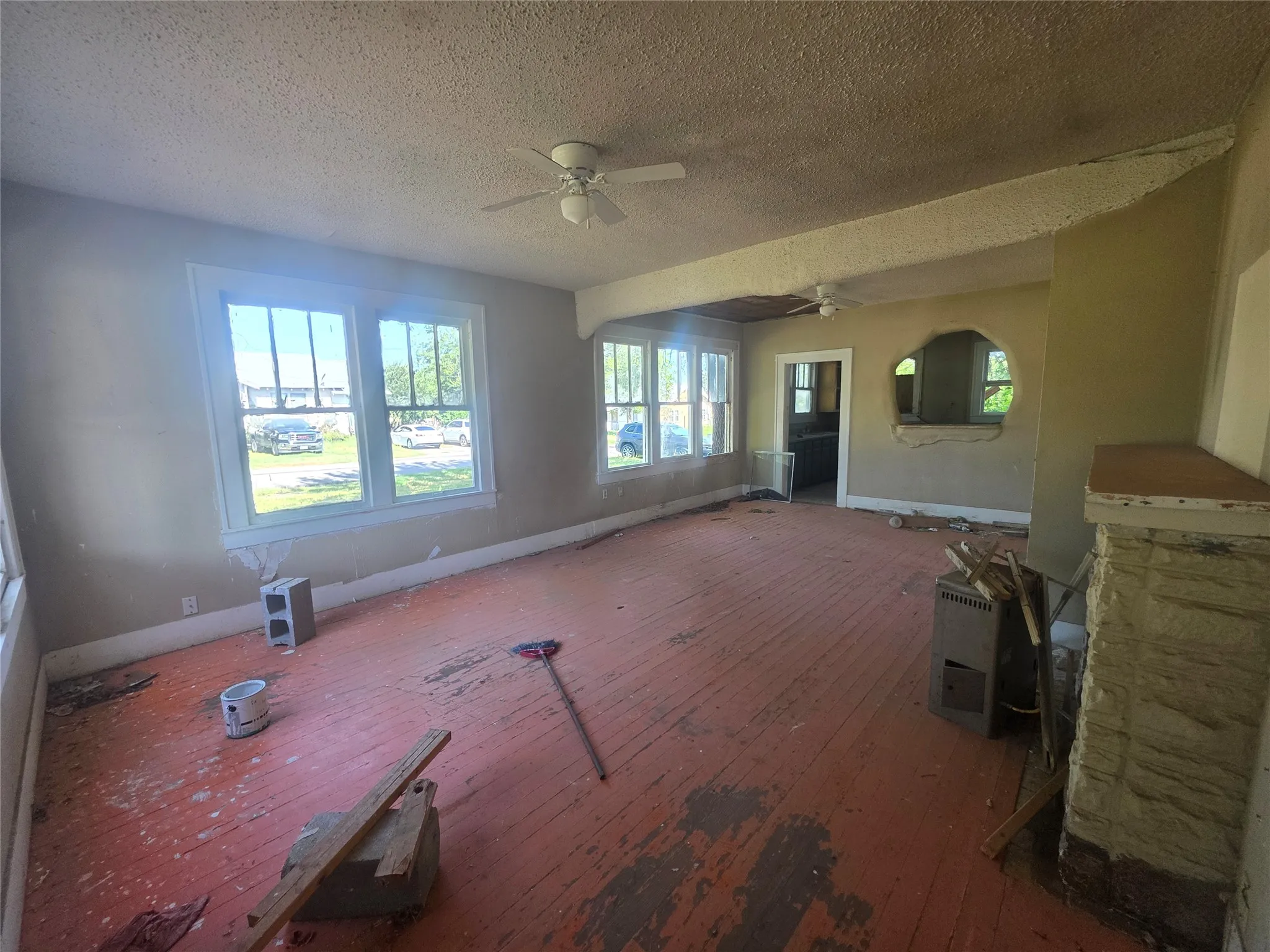 Spacious living area featuring multi-pane windows, a stone-clad fireplace structure, and exposed wood plank flooring