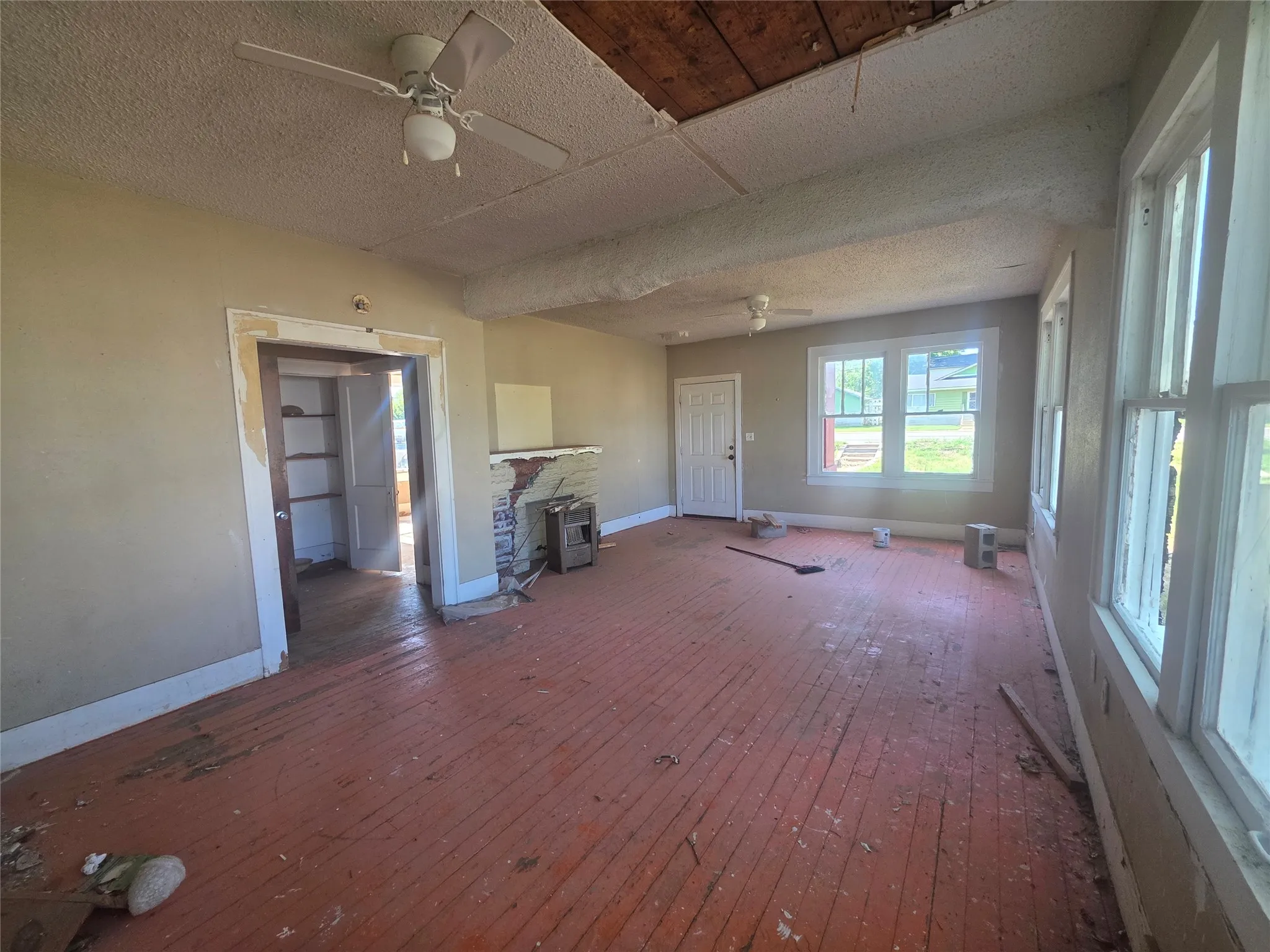 Spacious interior featuring wood-finish flooring, multiple windows, a ceiling fan, and a visible doorway with shelves beyond