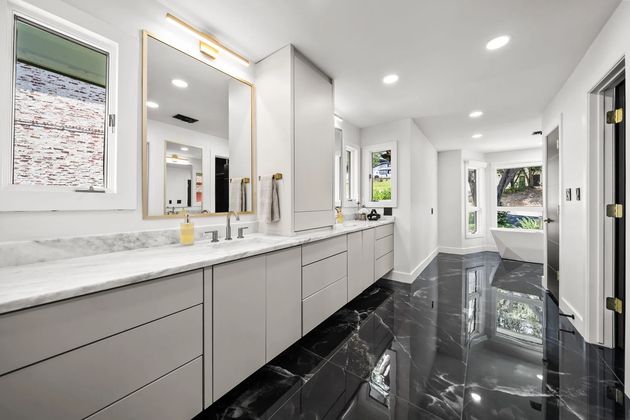 Spacious bathroom featuring large format black marble-effect flooring, a freestanding bathtub, recessed lighting, and a dual vanity with light gray cabinetry and a white countertop