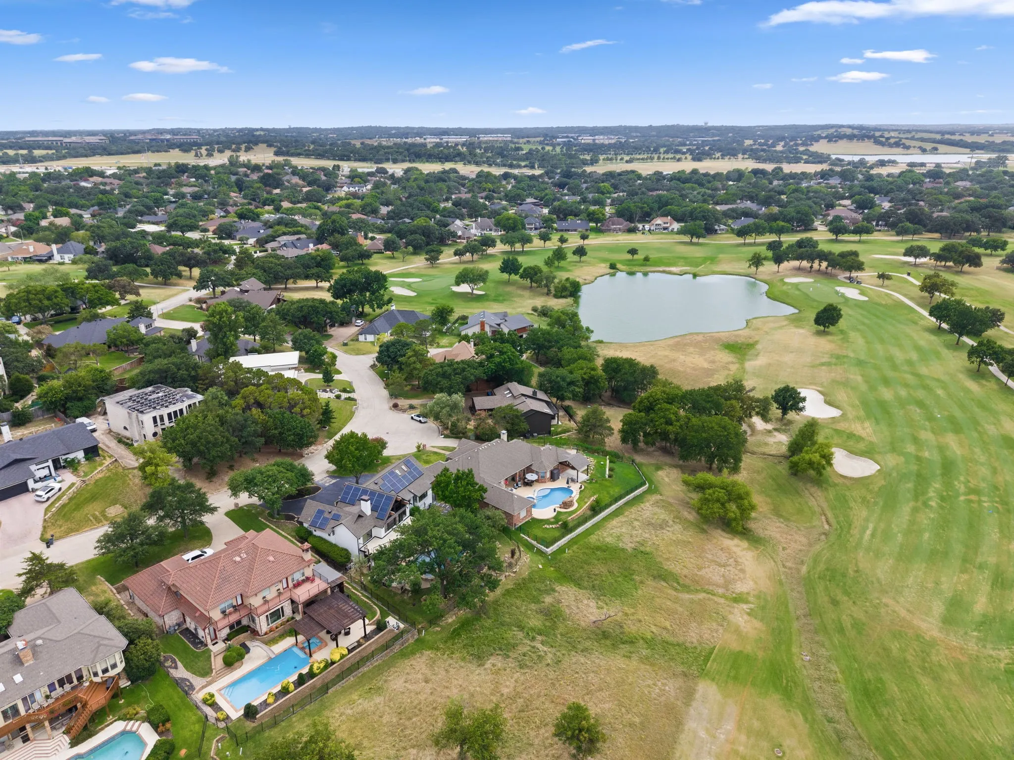 Expansive golf course community featuring homes with private swimming pools, mature trees, and a central pond