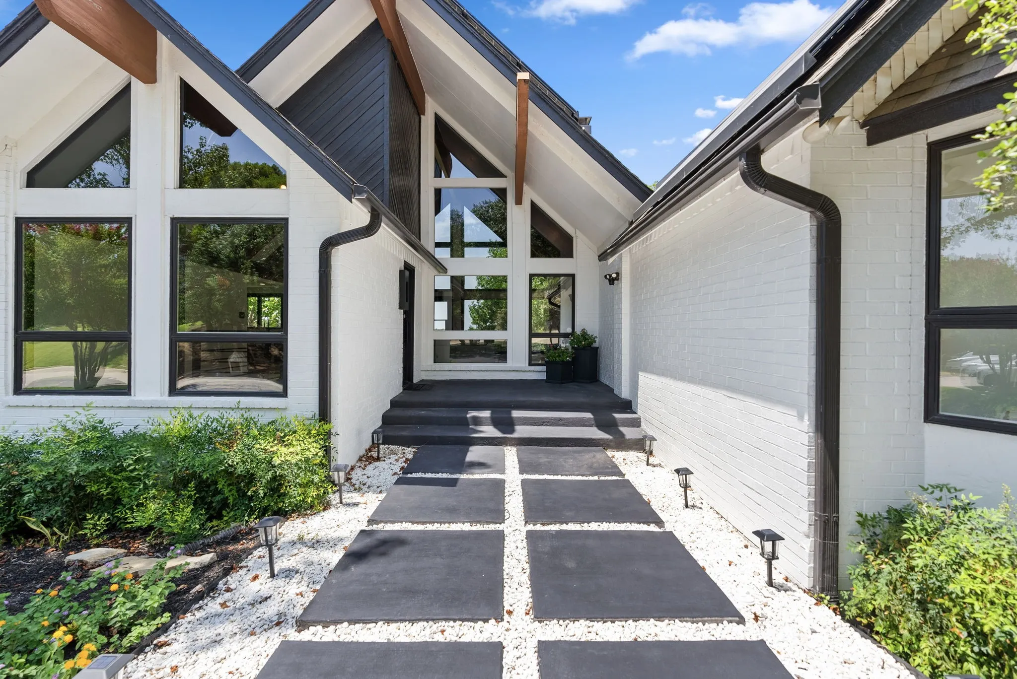 Modern architectural facade featuring white brick, dark trim, and a prominent peaked roofline