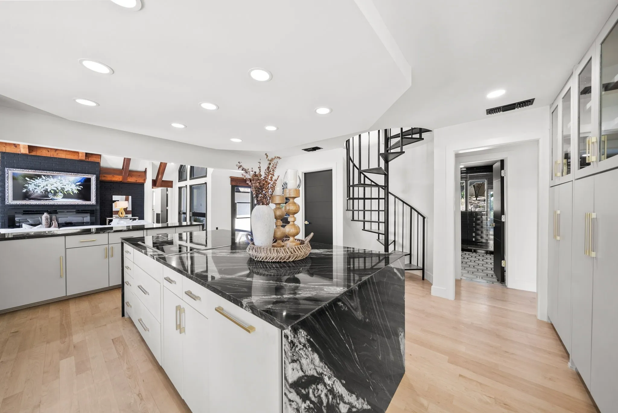 Spacious kitchen area featuring a large center island with a dark stone waterfall countertop, white cabinetry with gold-tone hardware, and light wood-finish flooring