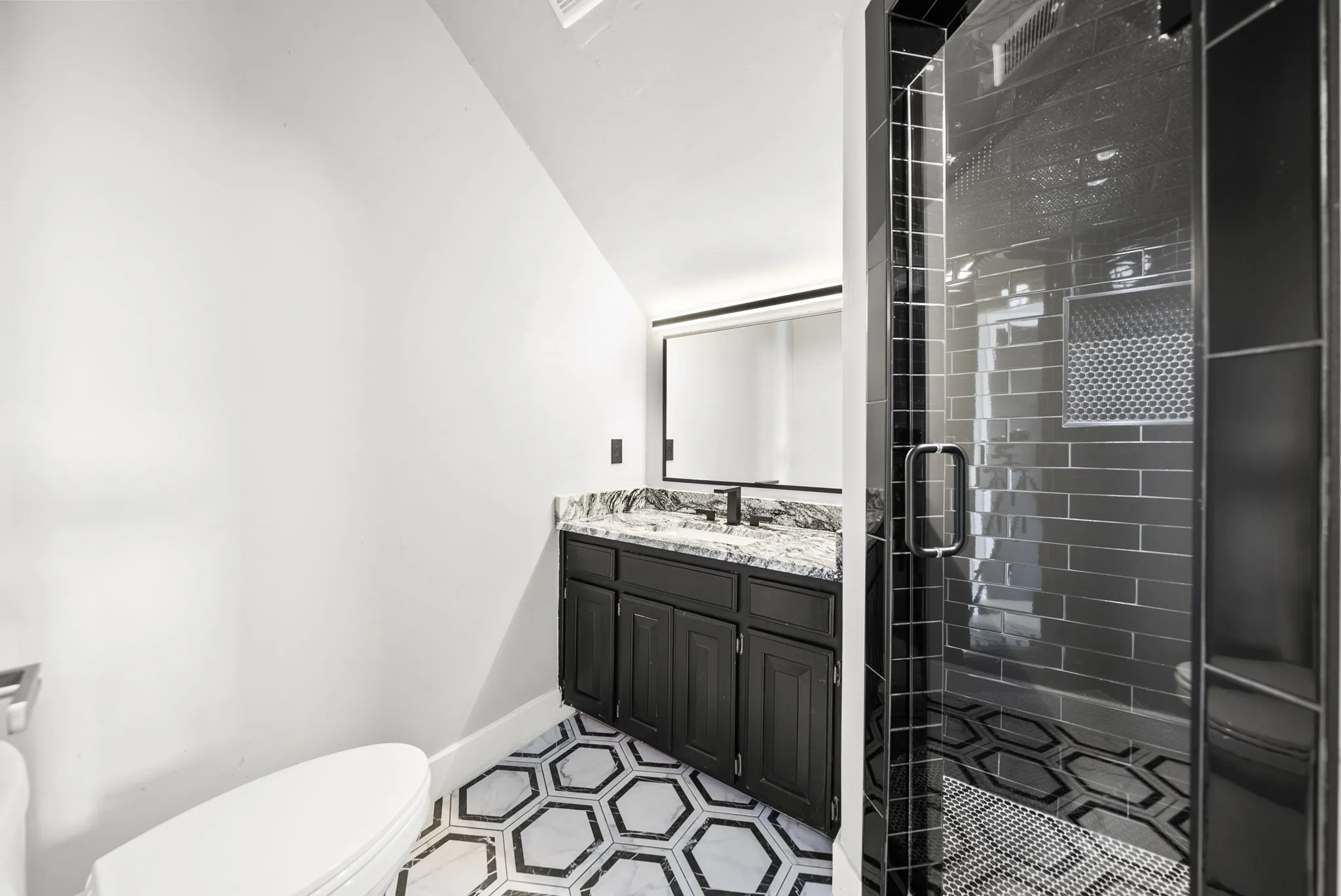 Bathroom featuring a black subway tile shower with glass enclosure, a vanity with dark cabinetry, stone countertop, and a black faucet, and a white and black hexagonal floor tile pattern