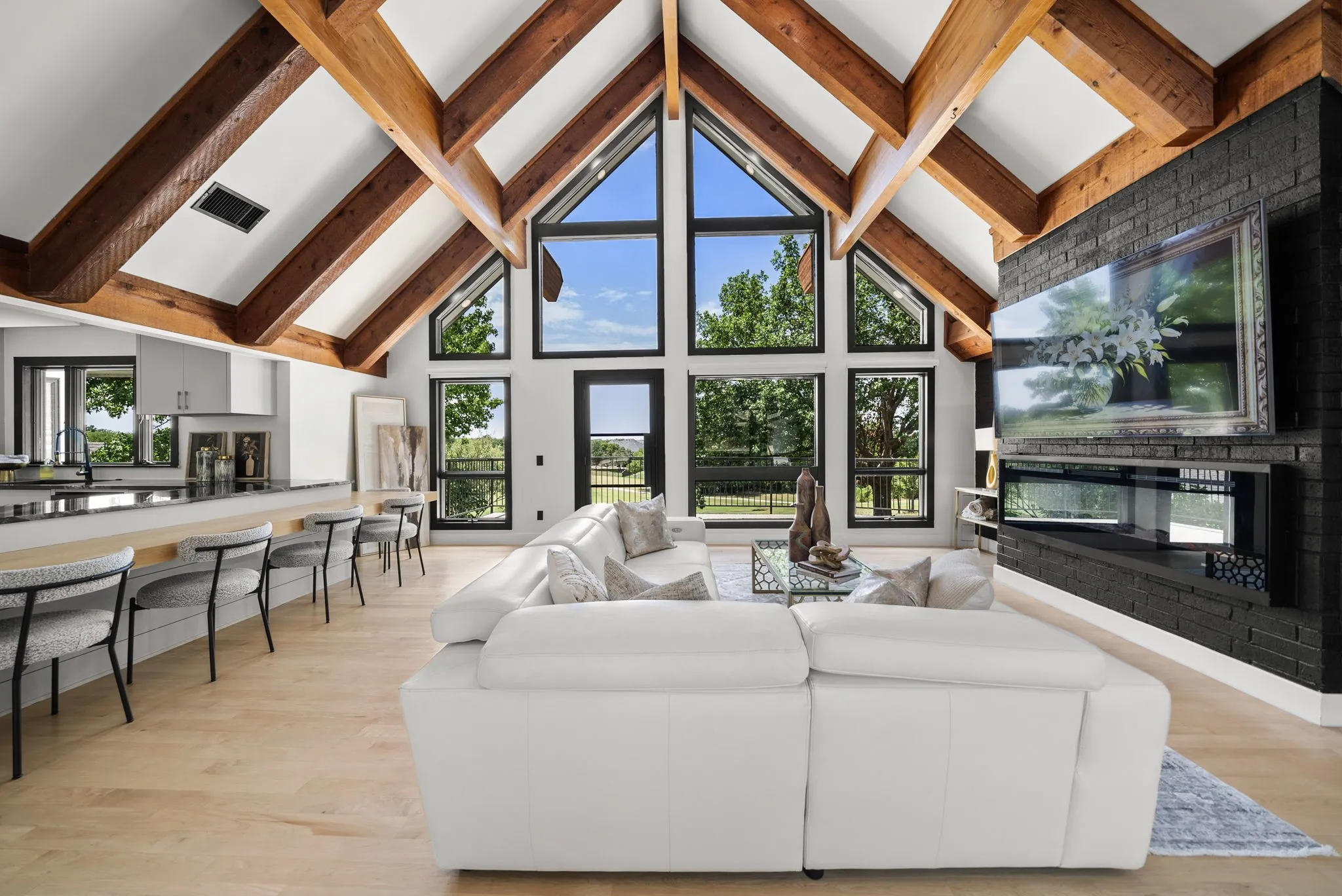 Spacious living area featuring a vaulted ceiling with exposed wooden beams, a floor-to-ceiling window wall, and light wood-finish flooring