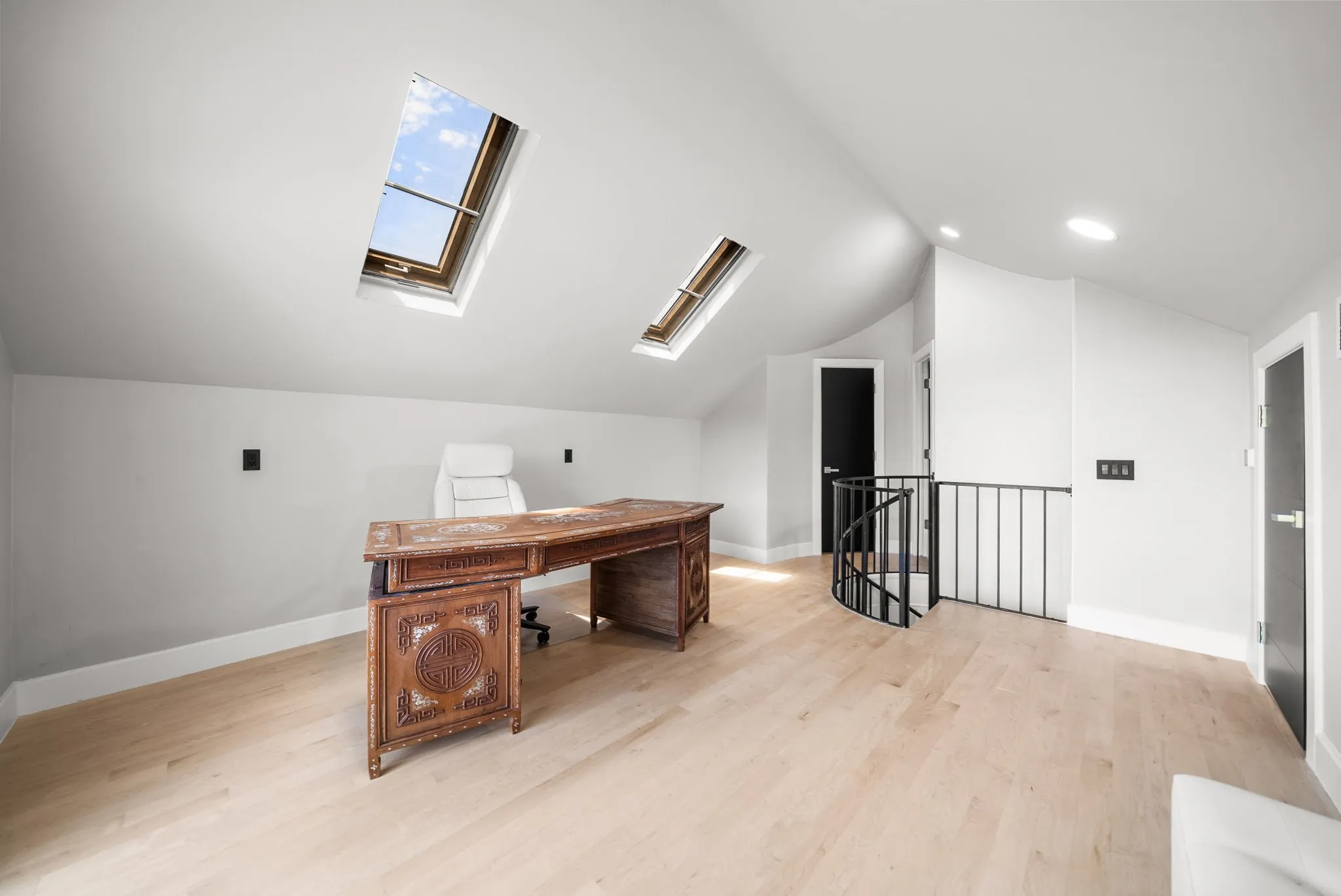 Open-concept room featuring light wood-finish flooring, two skylights, a spiral staircase with metal railing, and recessed ceiling lighting