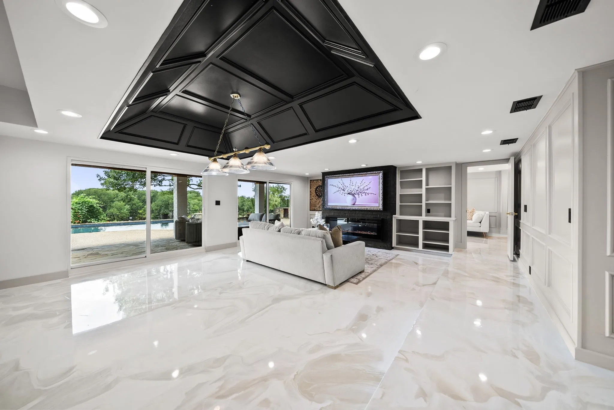 Spacious living area featuring polished marble-finish flooring, a coffered ceiling with recessed lighting, and a contemporary chandelier