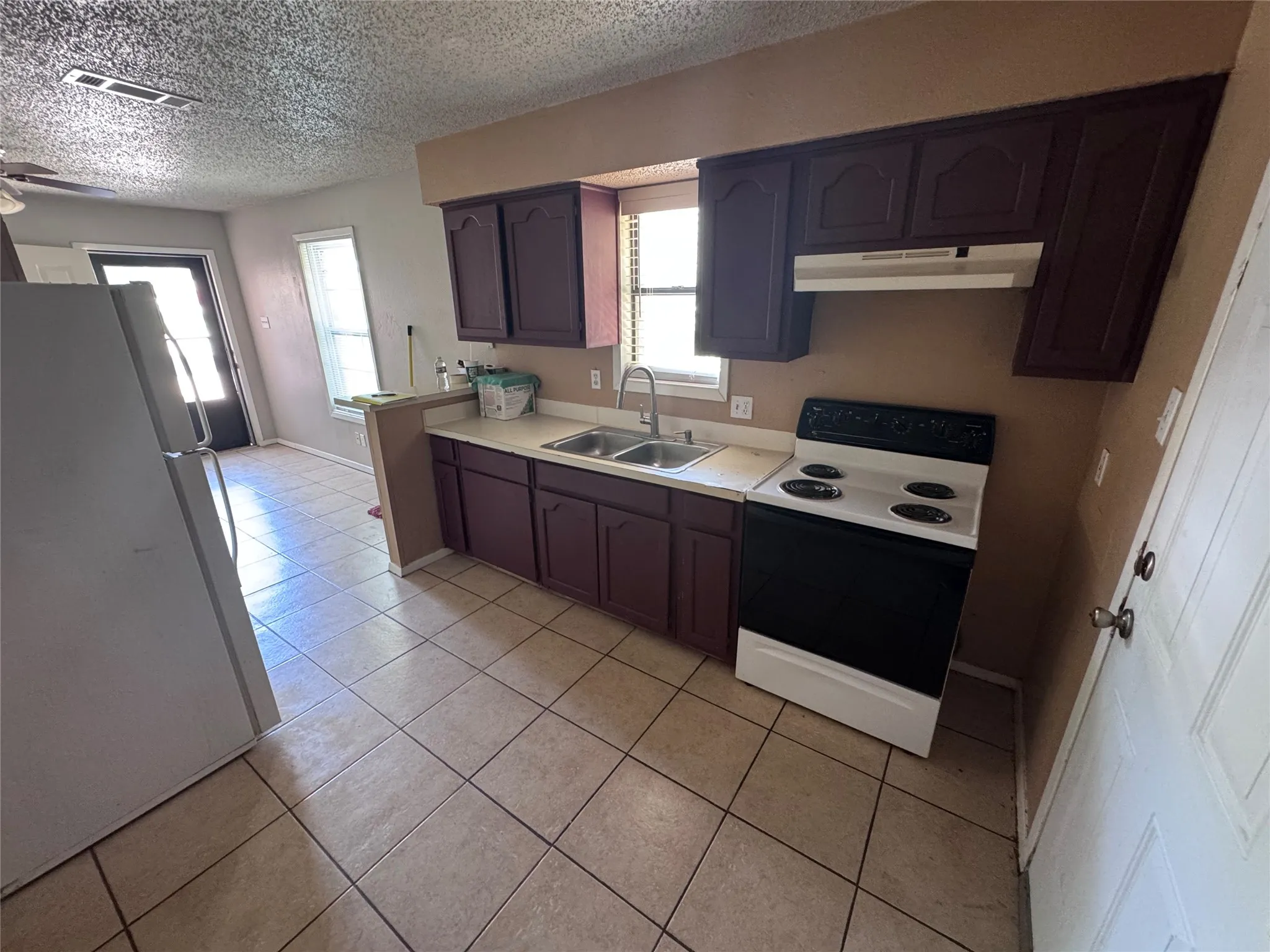 Kitchen featuring tile flooring, dark wood cabinetry, white countertops, and a white electric range with a range hood