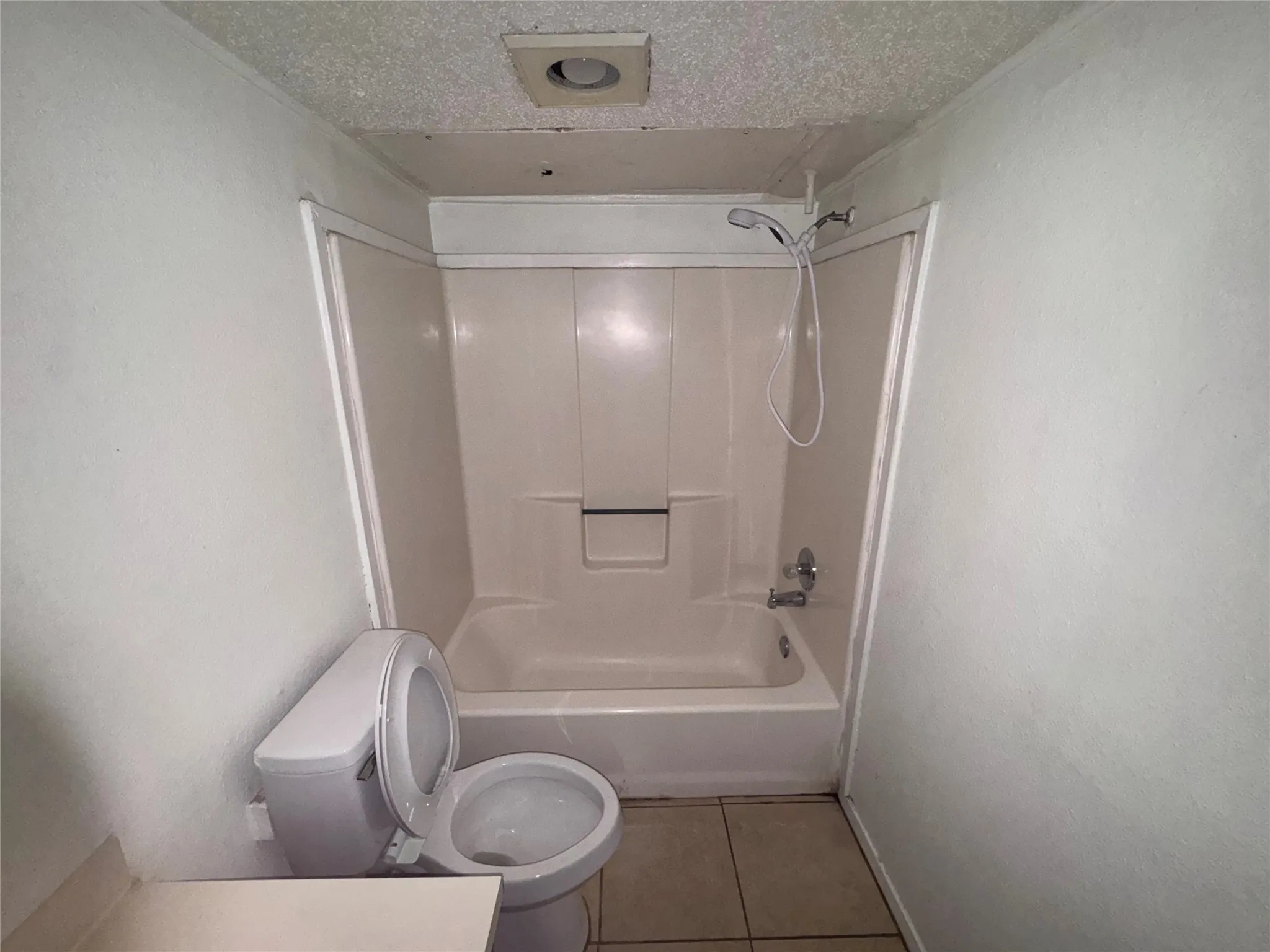 Bathroom featuring a white toilet, integrated tub and shower unit, and tiled flooring