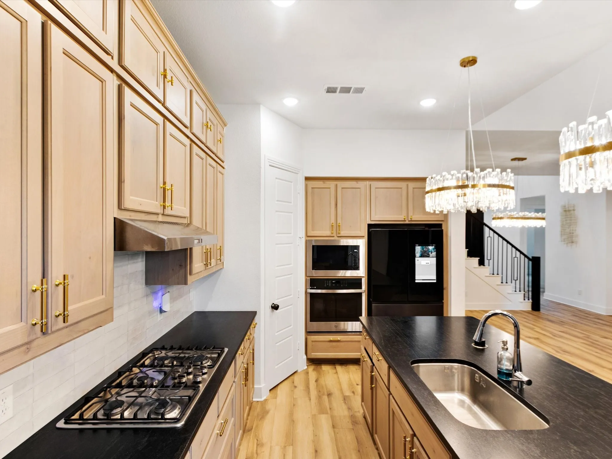 Contemporary kitchen featuring light wood cabinetry with gold-tone hardware, black countertops, and a gas cooktop