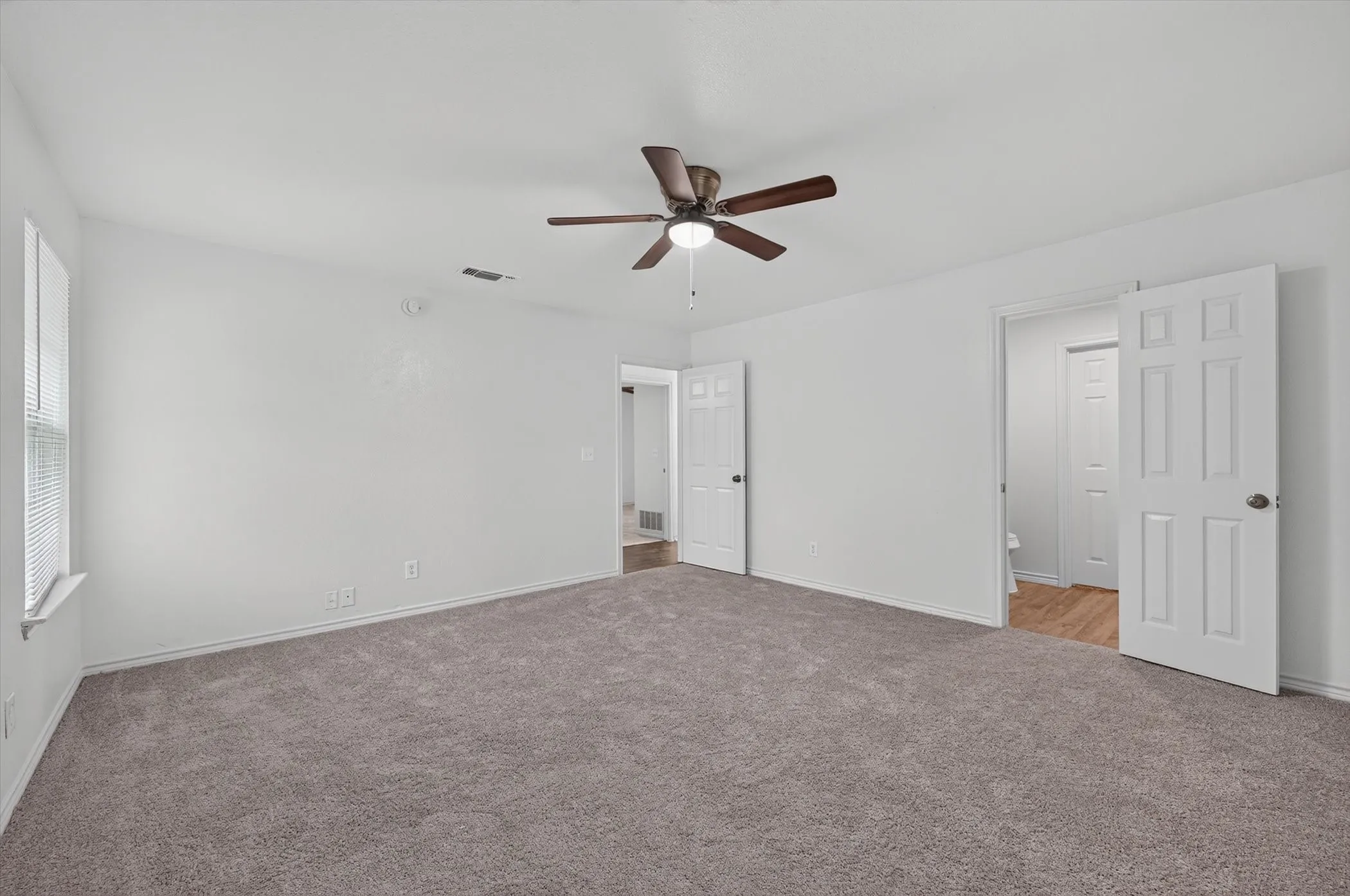 Spacious room featuring neutral carpet flooring, a ceiling fan with integrated lighting, and multiple panel doors