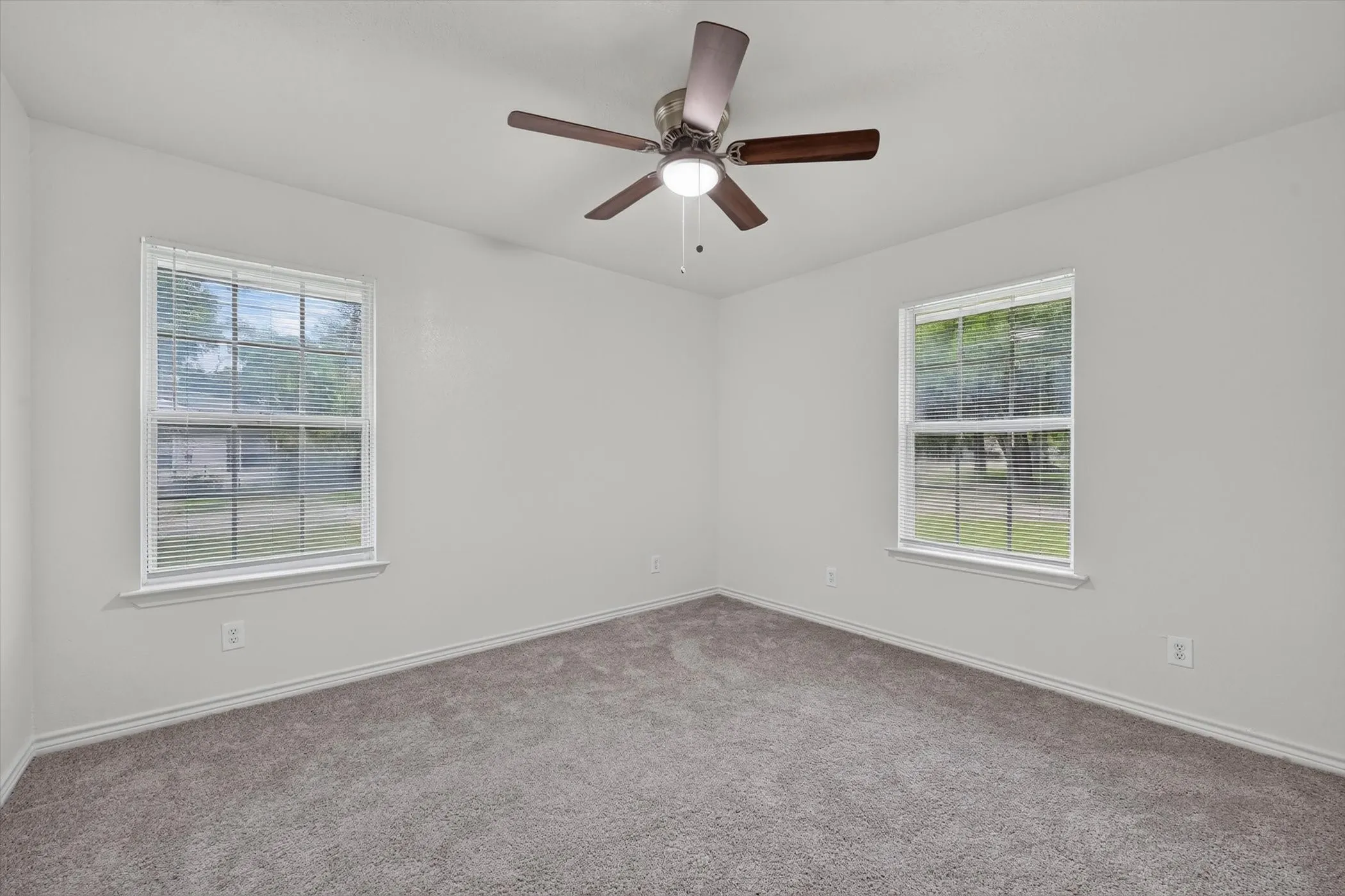 Carpeted room with white walls, two double-hung windows with blinds, a ceiling fan with integrated lighting, and white baseboards