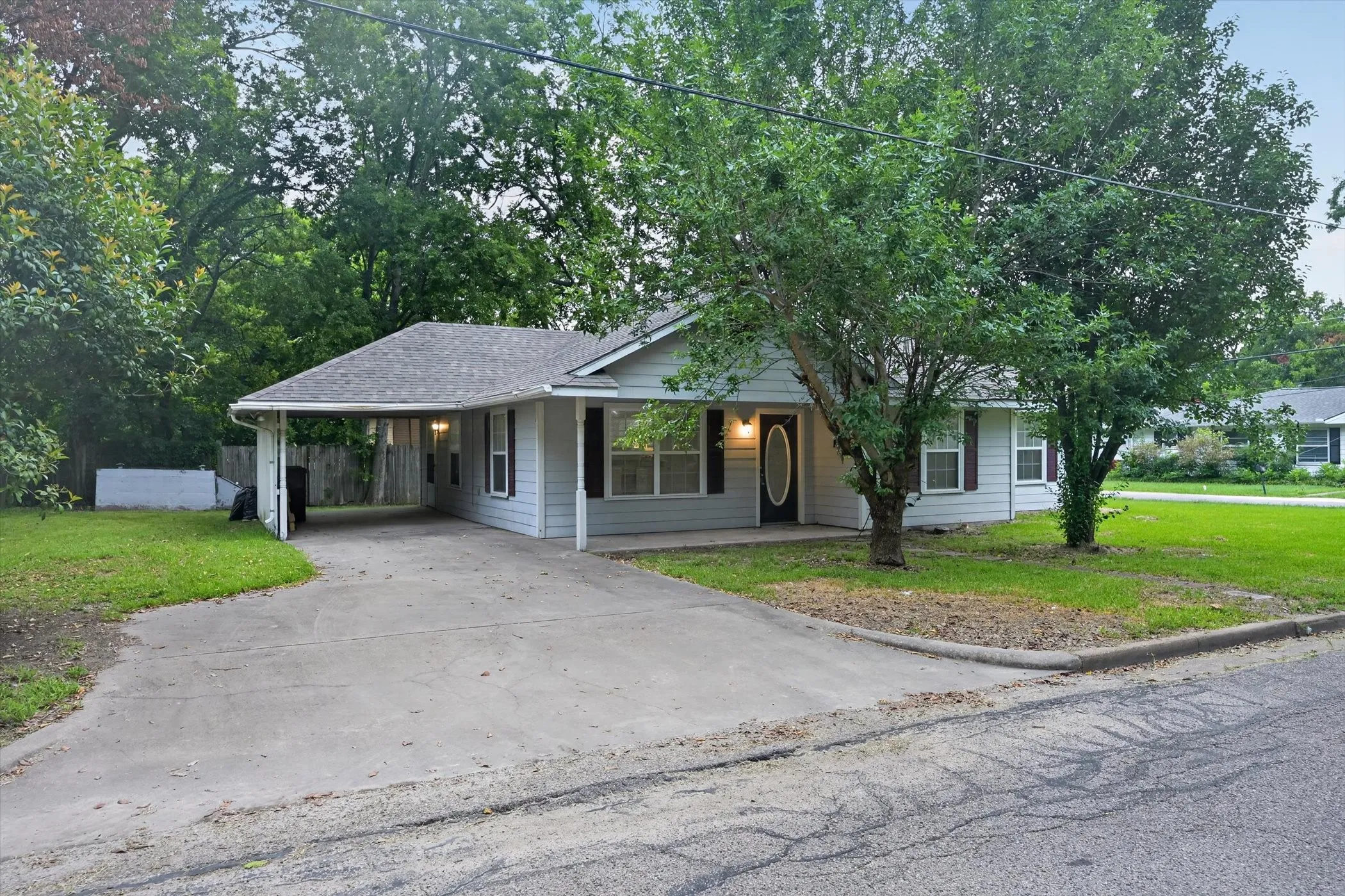 Single-story home featuring light grey siding, a dark asphalt shingle roof, and a prominent carport