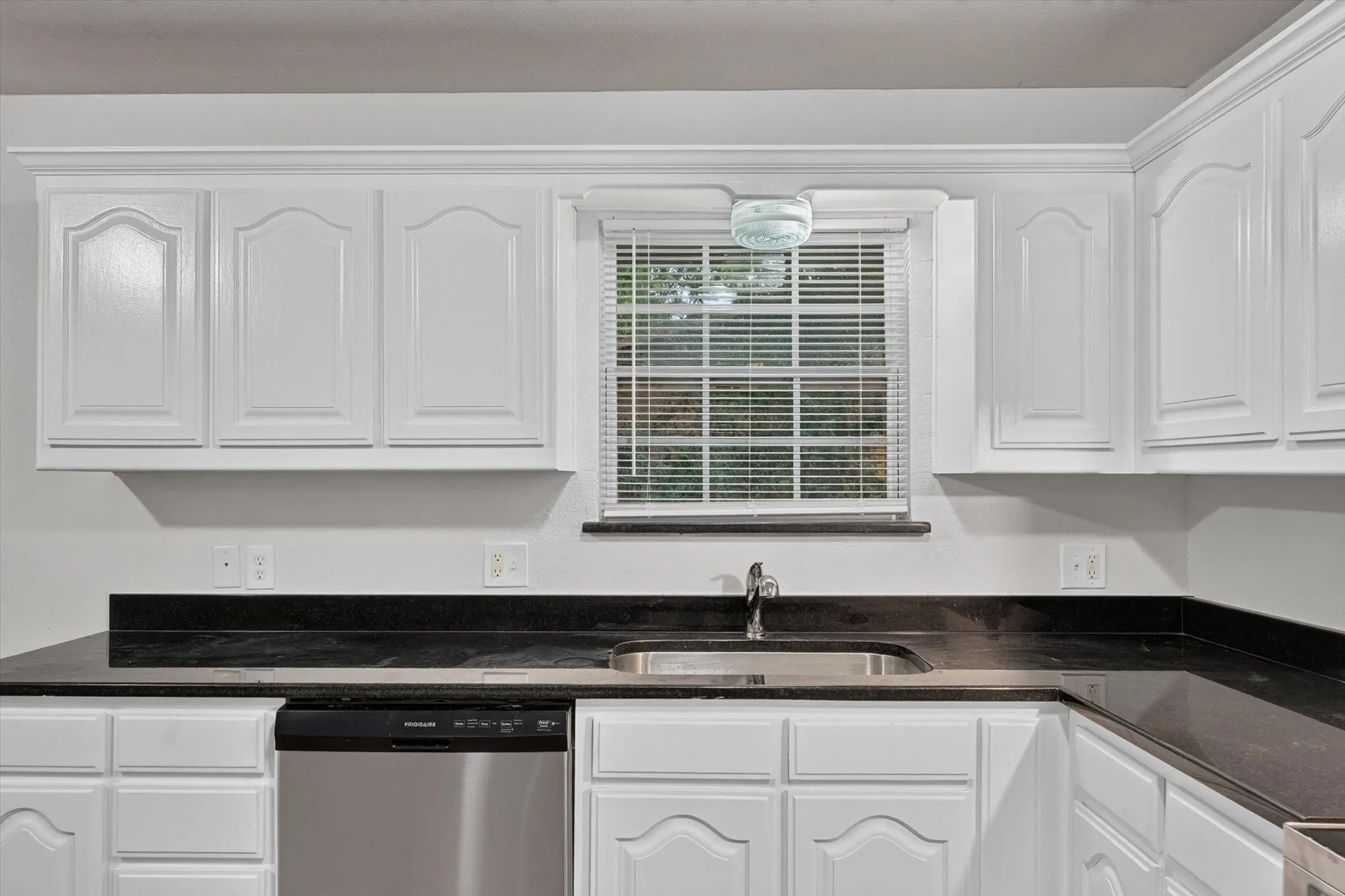 Kitchen featuring white paneled cabinetry, dark countertops, a stainless steel sink, and a stainless steel dishwasher