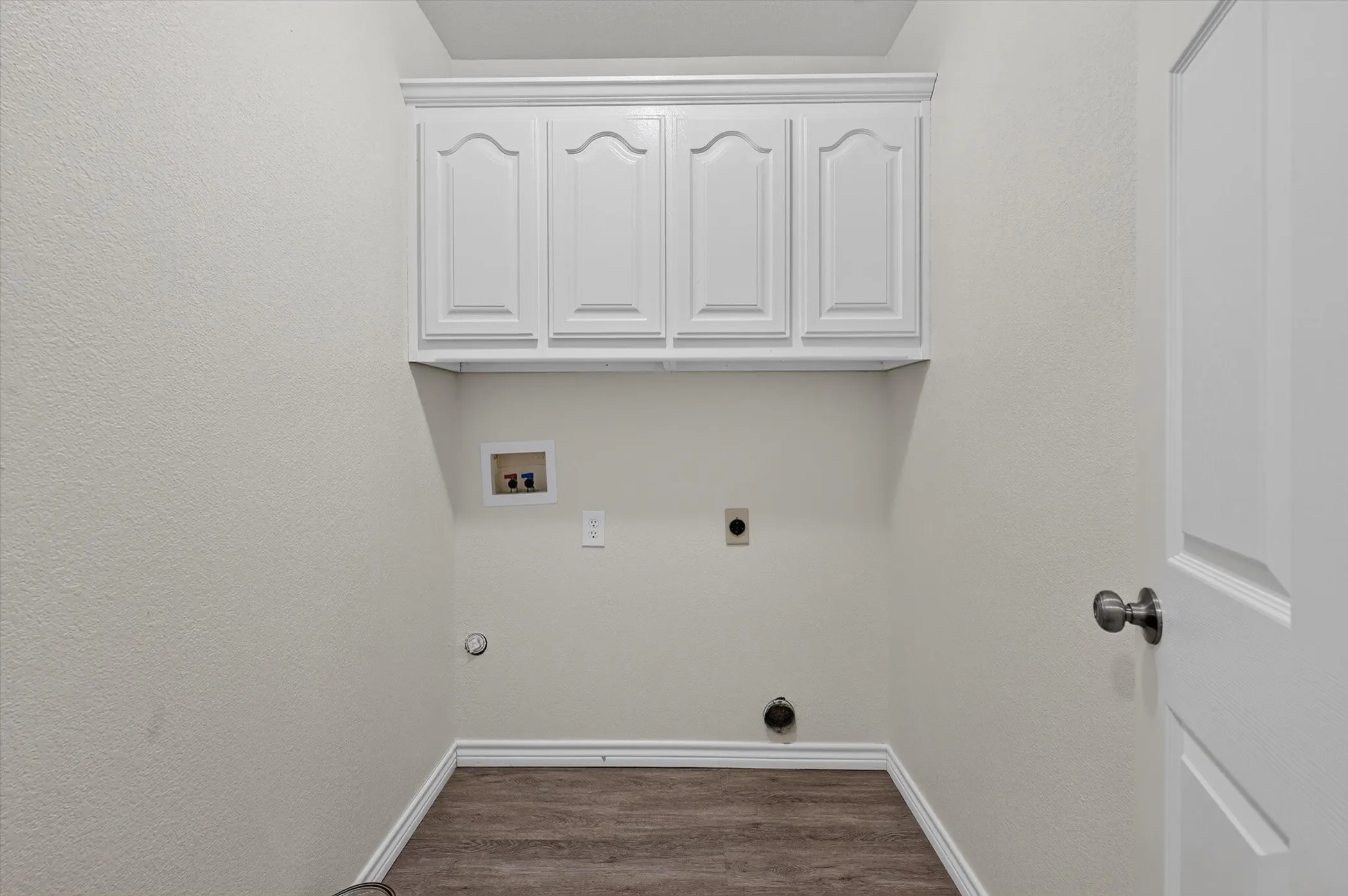 Utility area featuring overhead white cabinetry, wood-finish flooring, and white baseboards