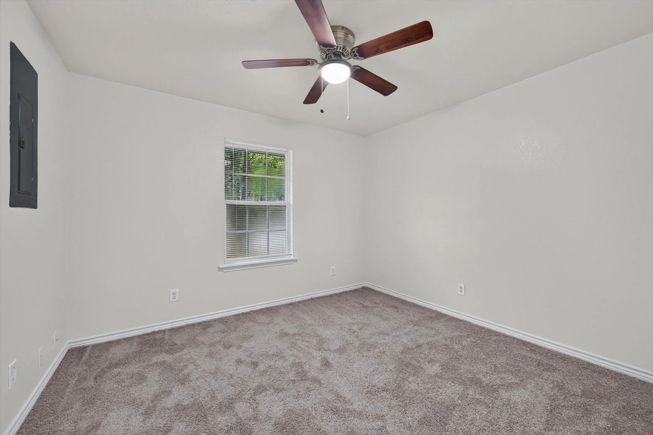 Carpeted room featuring a ceiling fan with light fixture, a window with exterior tree views, and a neutral wall color