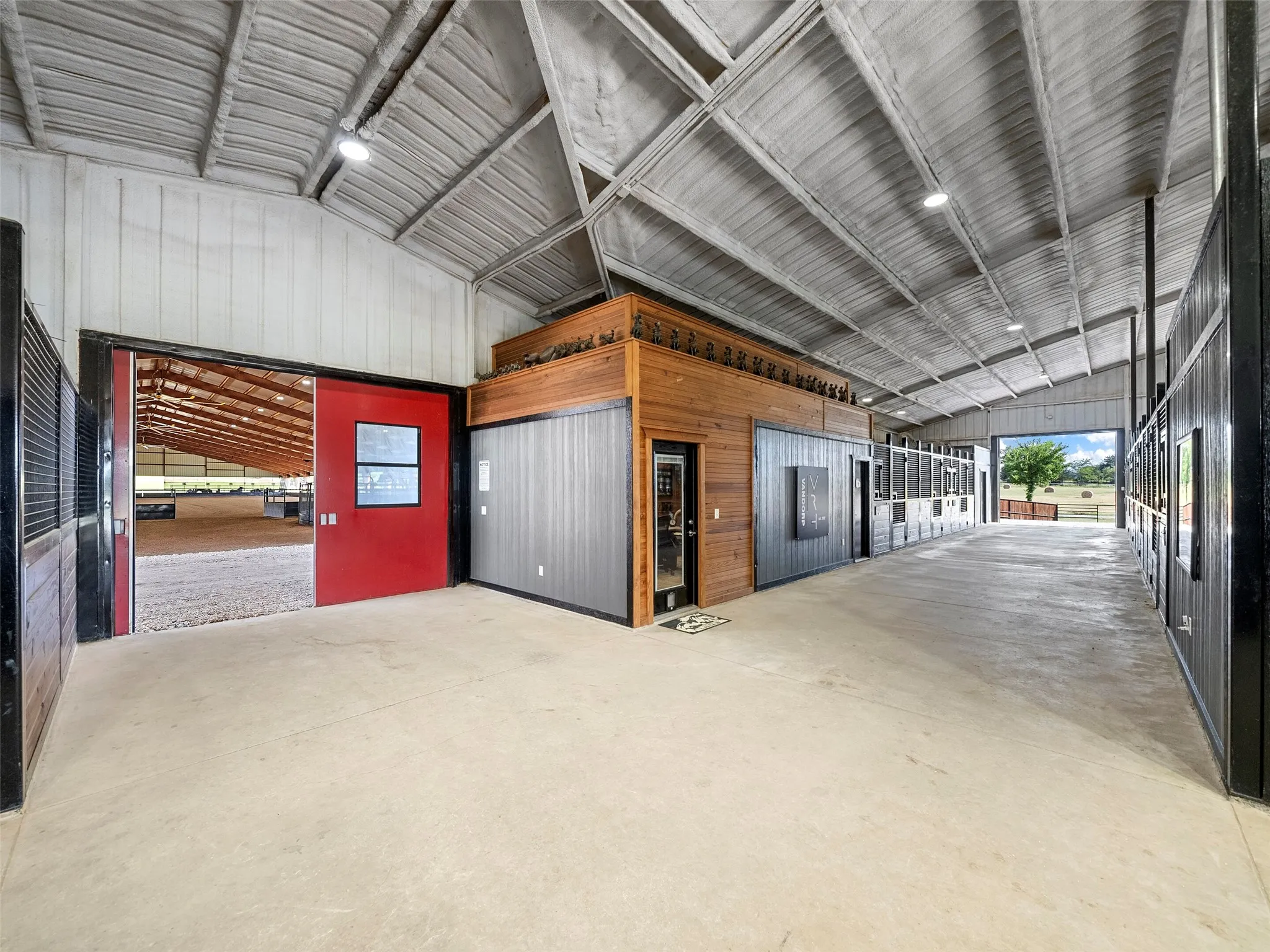 MAIN BARN INTERIOR...Views Of Aisle 1, Featuring An Office, And A Bathroom With Washer/Dryer Hookups. Cvrd Breezeway Behind Red Doors Leads Into Covered Arena