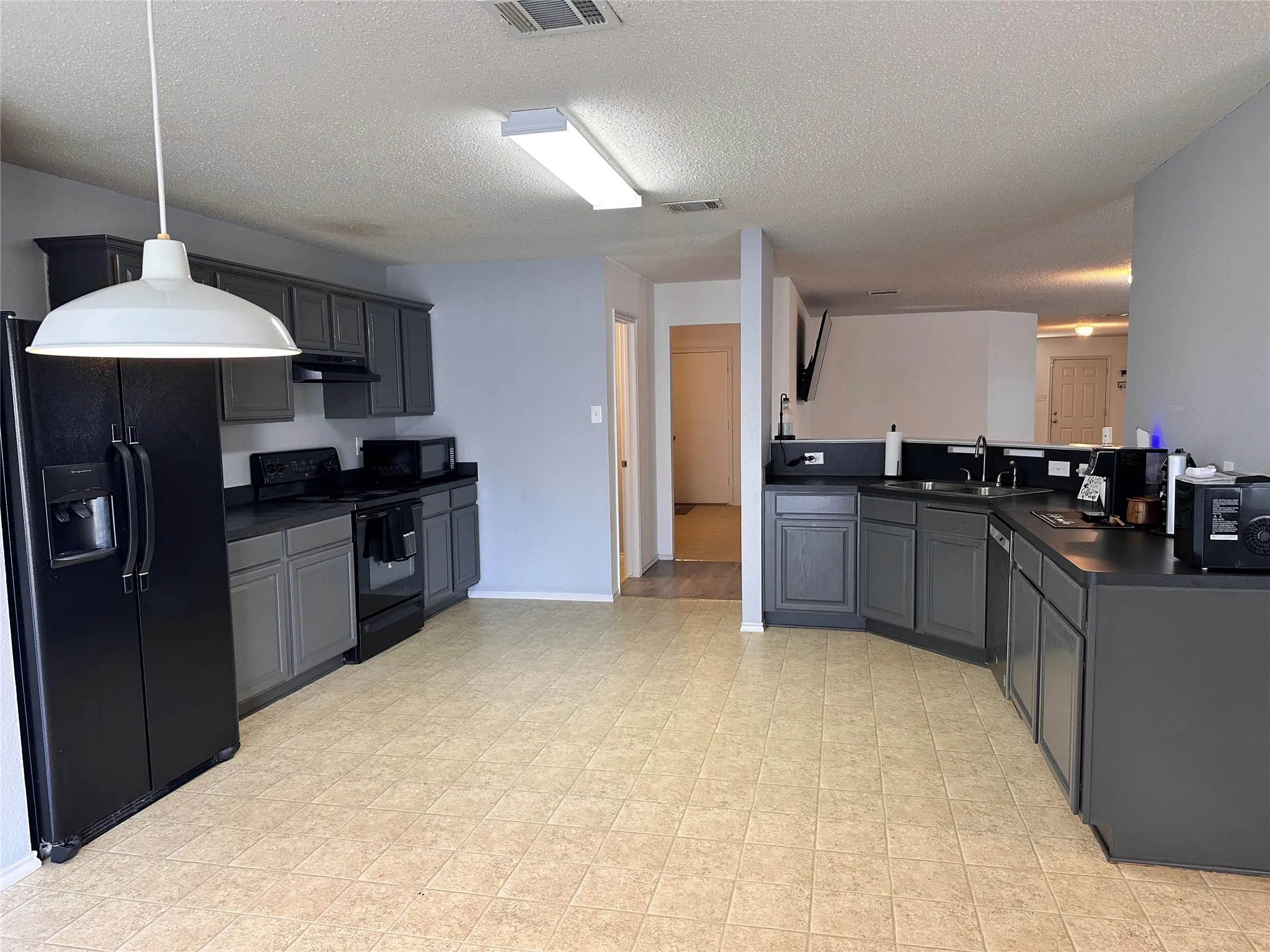 Kitchen featuring dark cabinetry, dark countertops, a double-basin stainless steel sink, and tile flooring