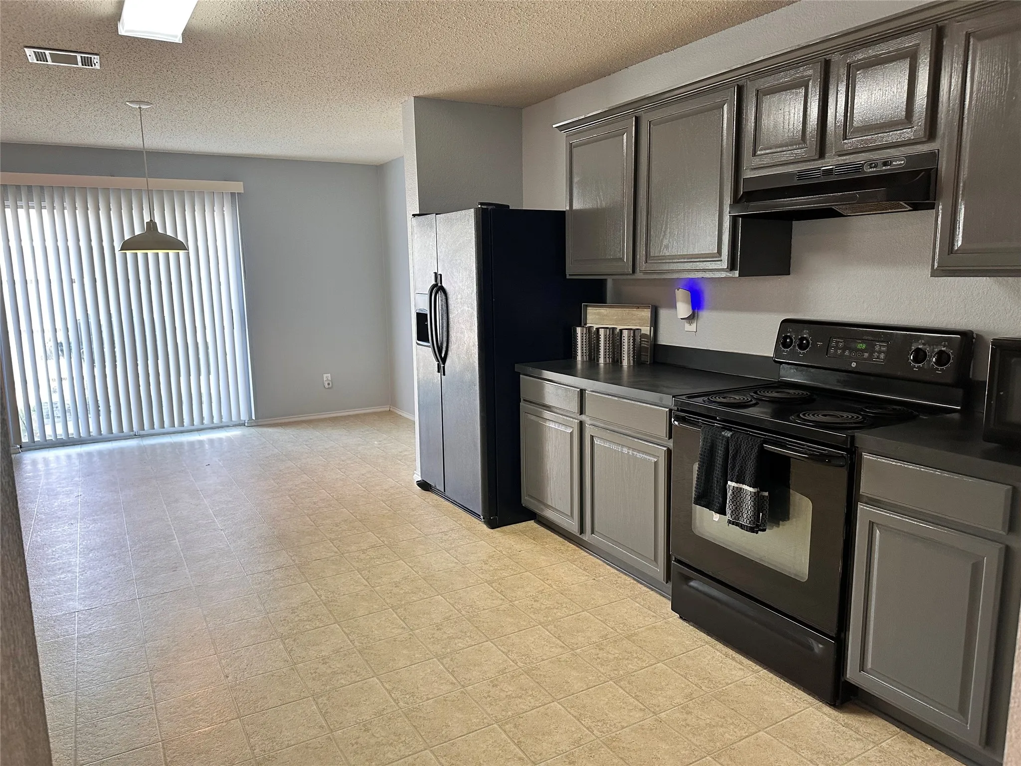 Kitchen featuring gray cabinetry, black appliances, dark countertops, and tile flooring