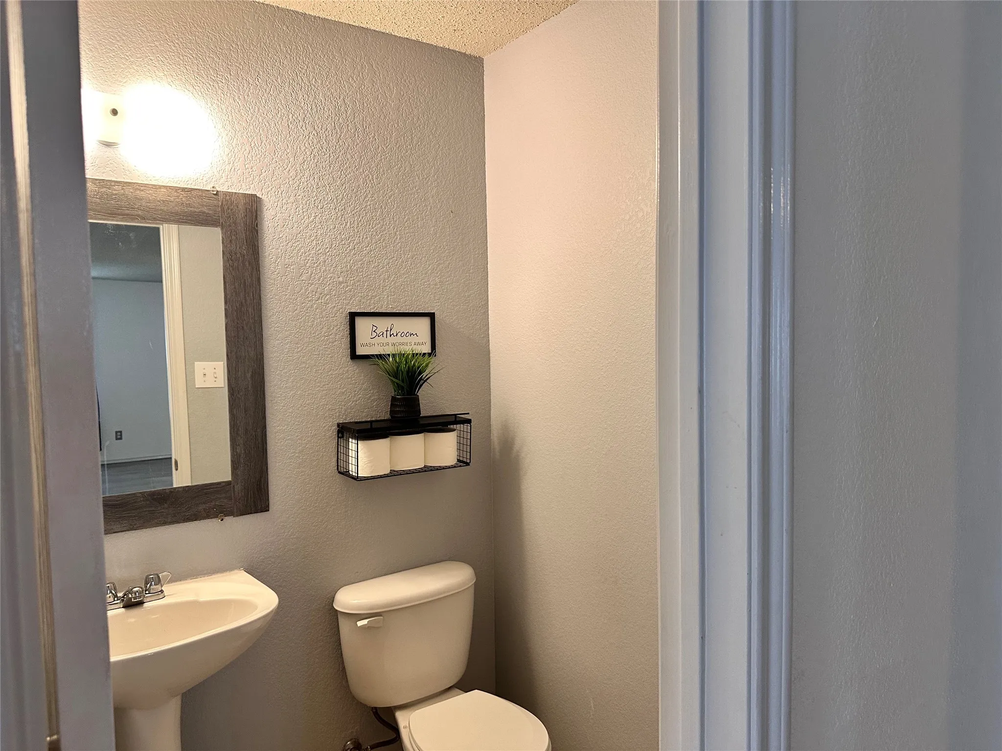 Pedestal sink, wall-mounted mirror with a distressed wood frame, and a toilet with a traditional tank