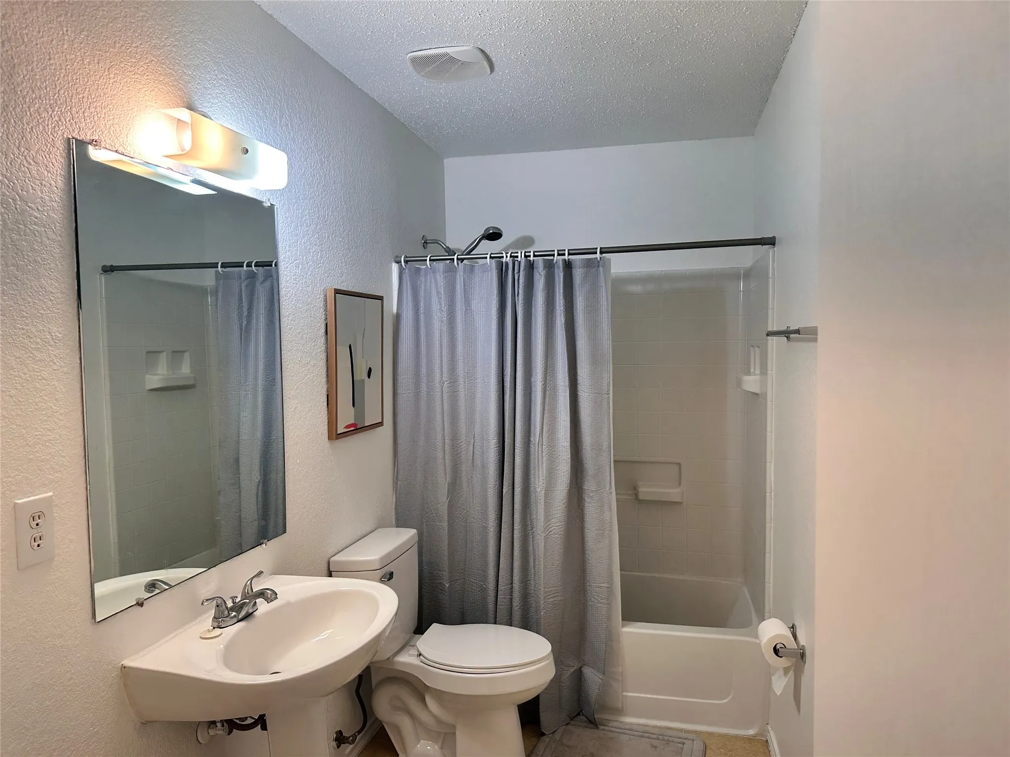 Pedestal sink with chrome faucet, wall-mounted mirror, white toilet, and tub-shower combination with integrated shelving