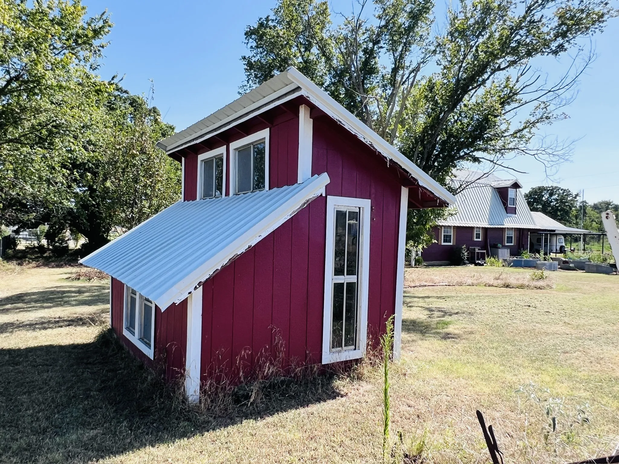 Red-painted outbuilding featuring a sloped metal roof awning, white trim, and multiple windows