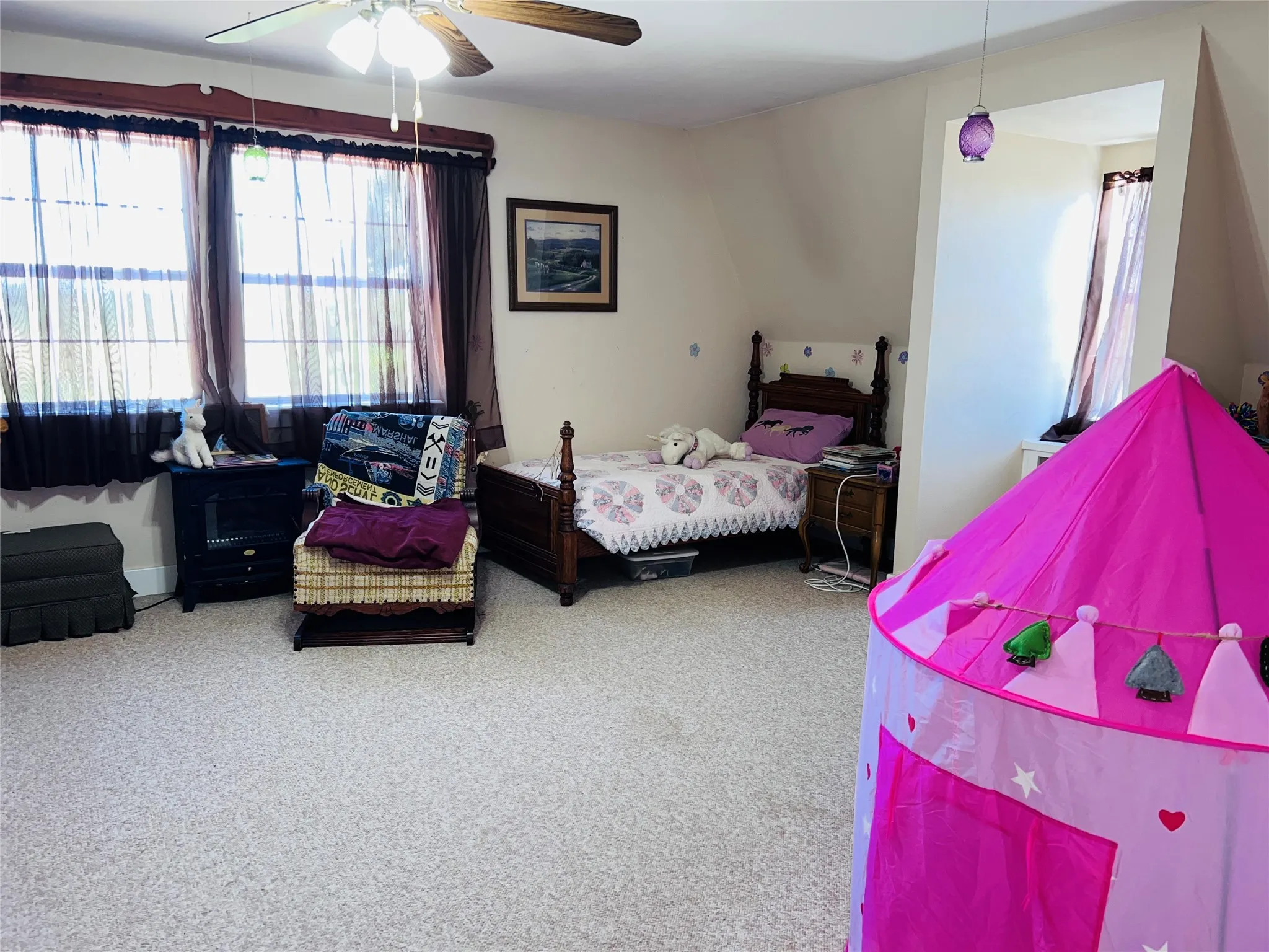 Upstairs large carpeted bedroom featuring a ceiling fan with light fixture, multiple windows, a recessed area, and sloped ceilings