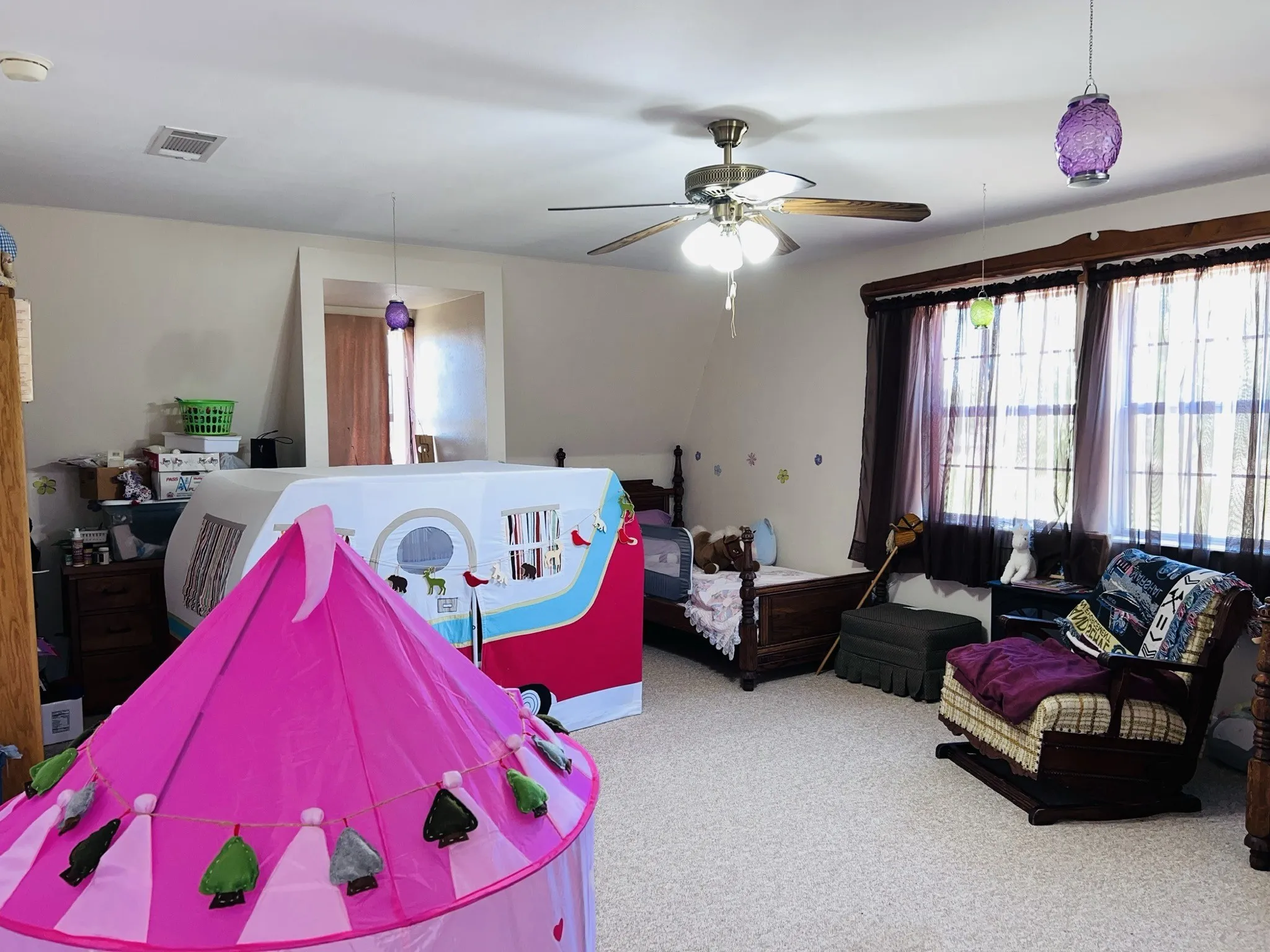 Upstairs carpeted bedroom featuring a ceiling fan with light fixture, multiple windows with dark window treatments
