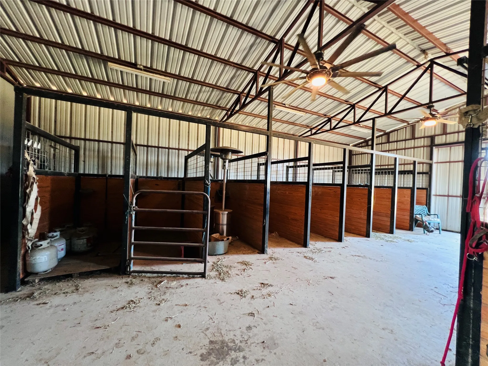 Barn interior featuring nine standing stalls with wood-finish paneling, metal gates, and corrugated metal walls
