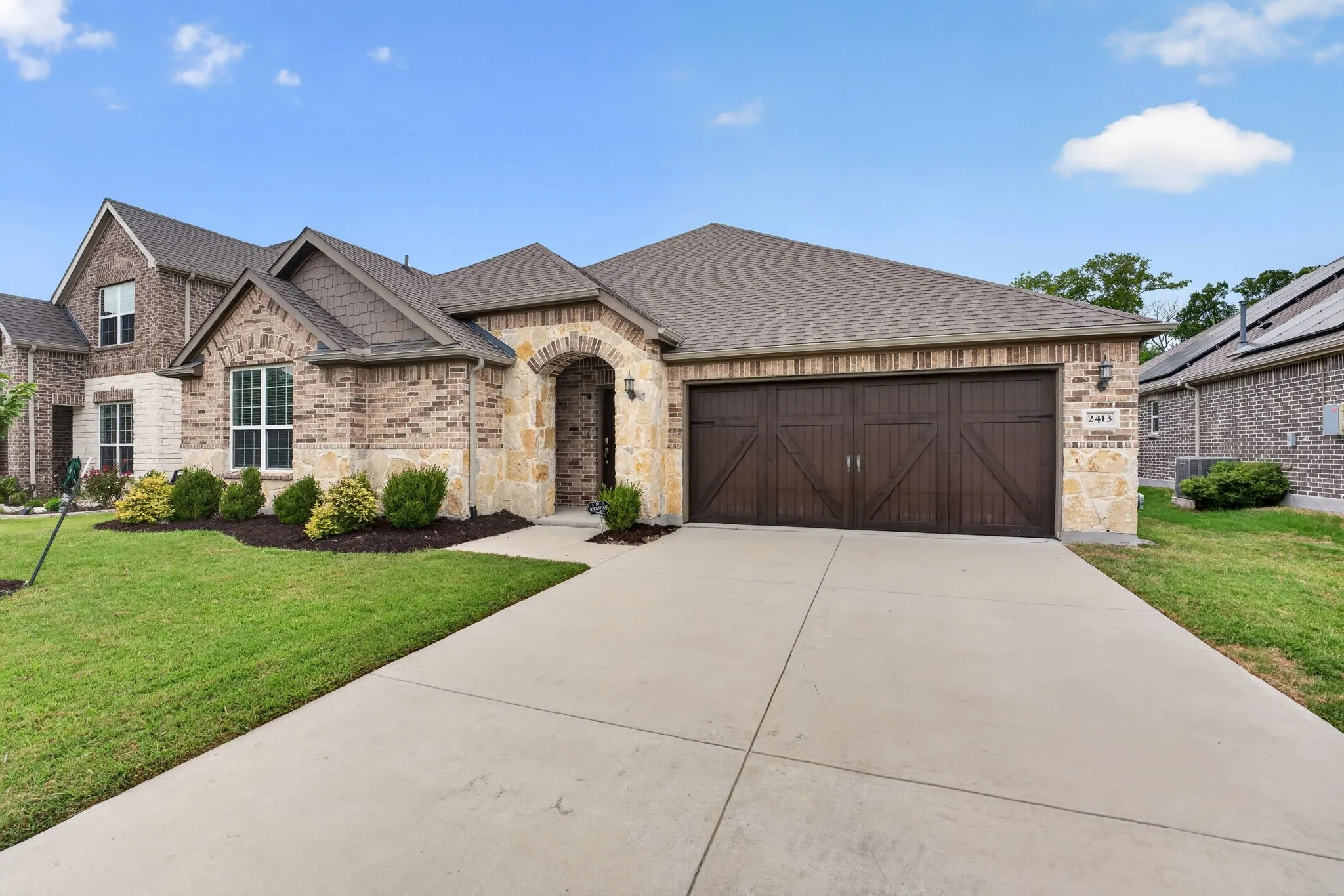 Brick and stone facade residence featuring a dark wood-finish garage door