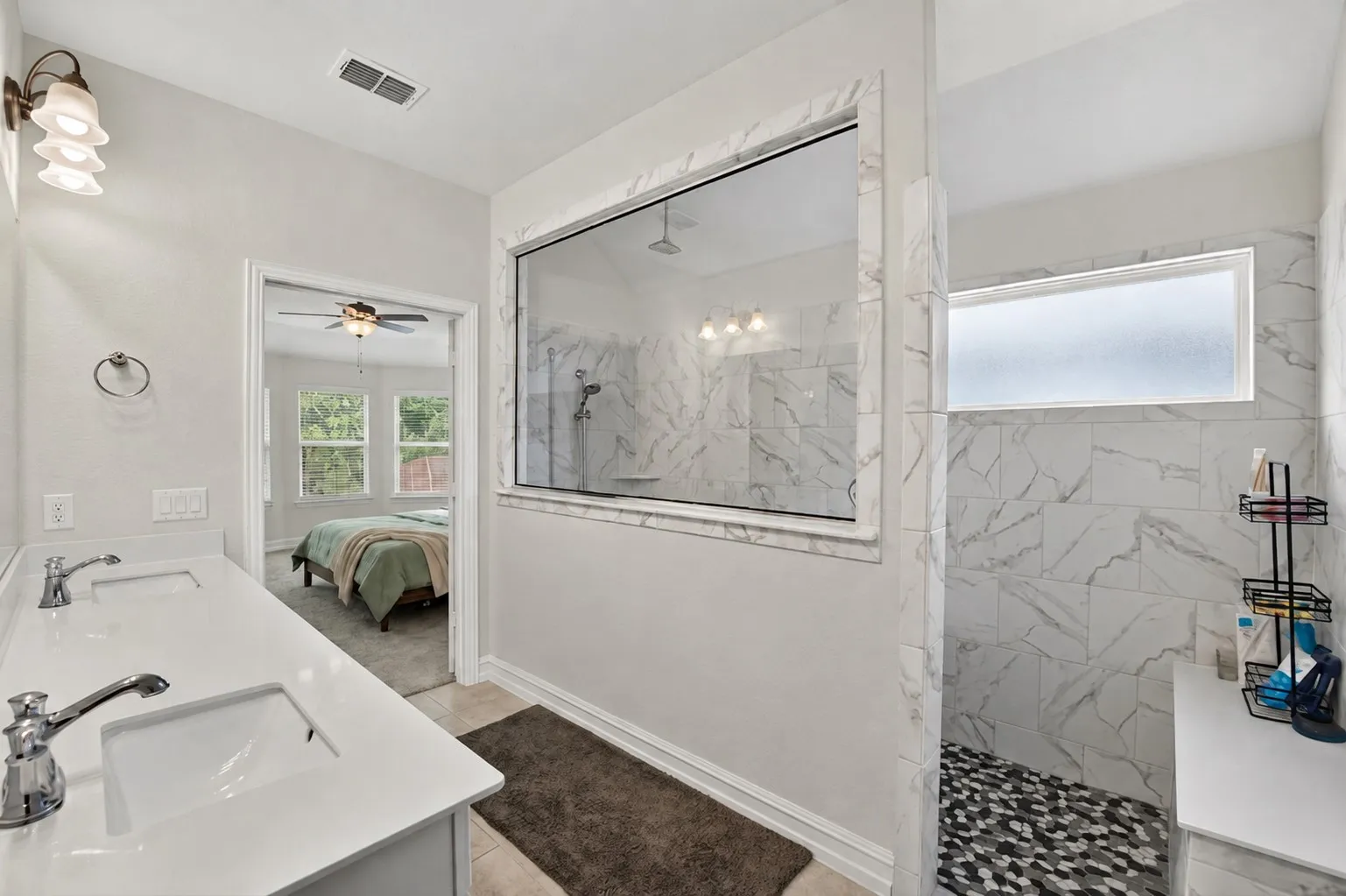Spa-inspired primary bathroom featuring a marble-clad walk-in shower with frameless glass enclosure, dual vanity with polished countertop and chrome fixtures, heated floor, recessed lighting, and a soaking tub positioned to overlook the bedroom beyond