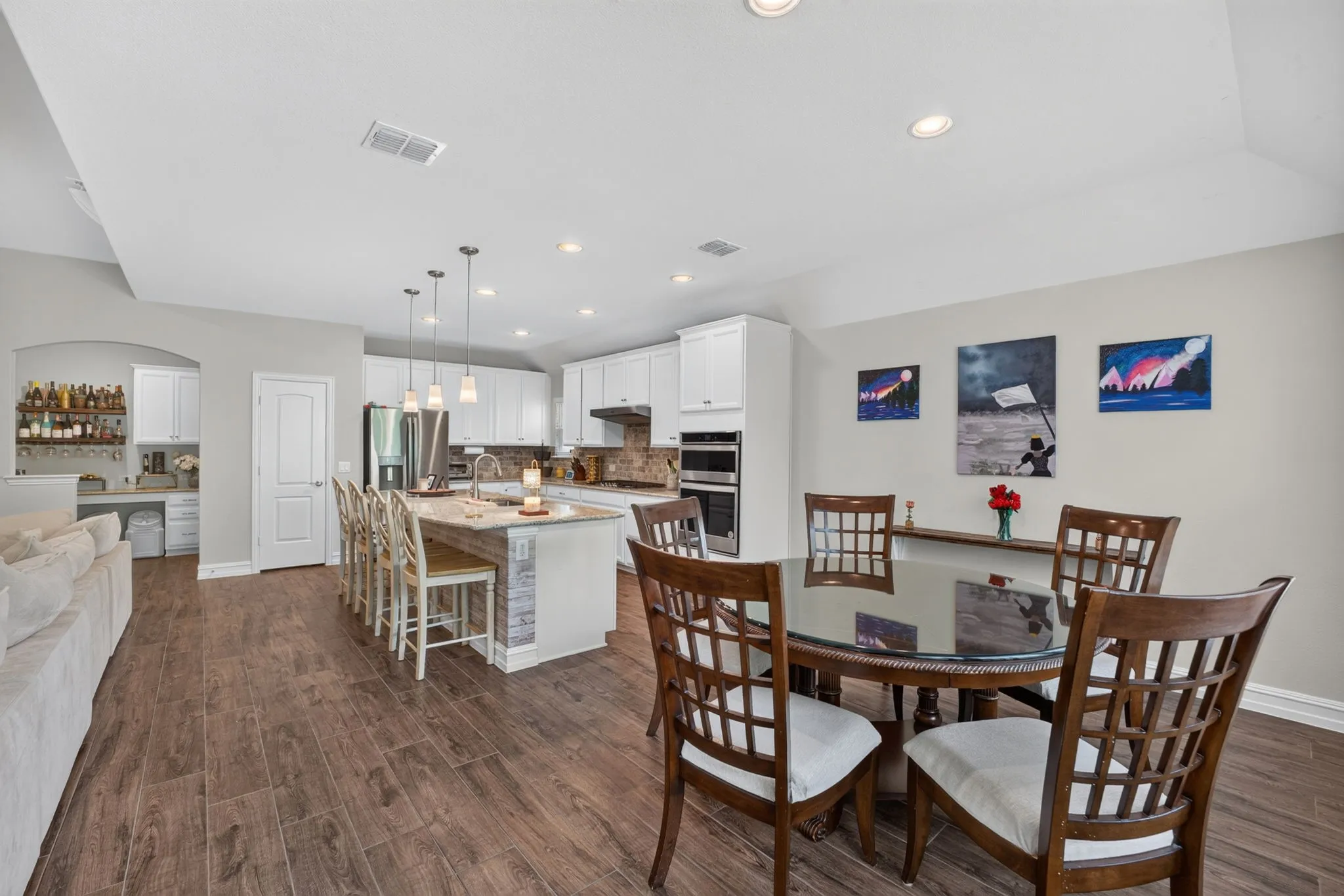 Spacious kitchen featuring white cabinetry, stainless steel appliances, a center island with pendant lighting, and wood-finish flooring