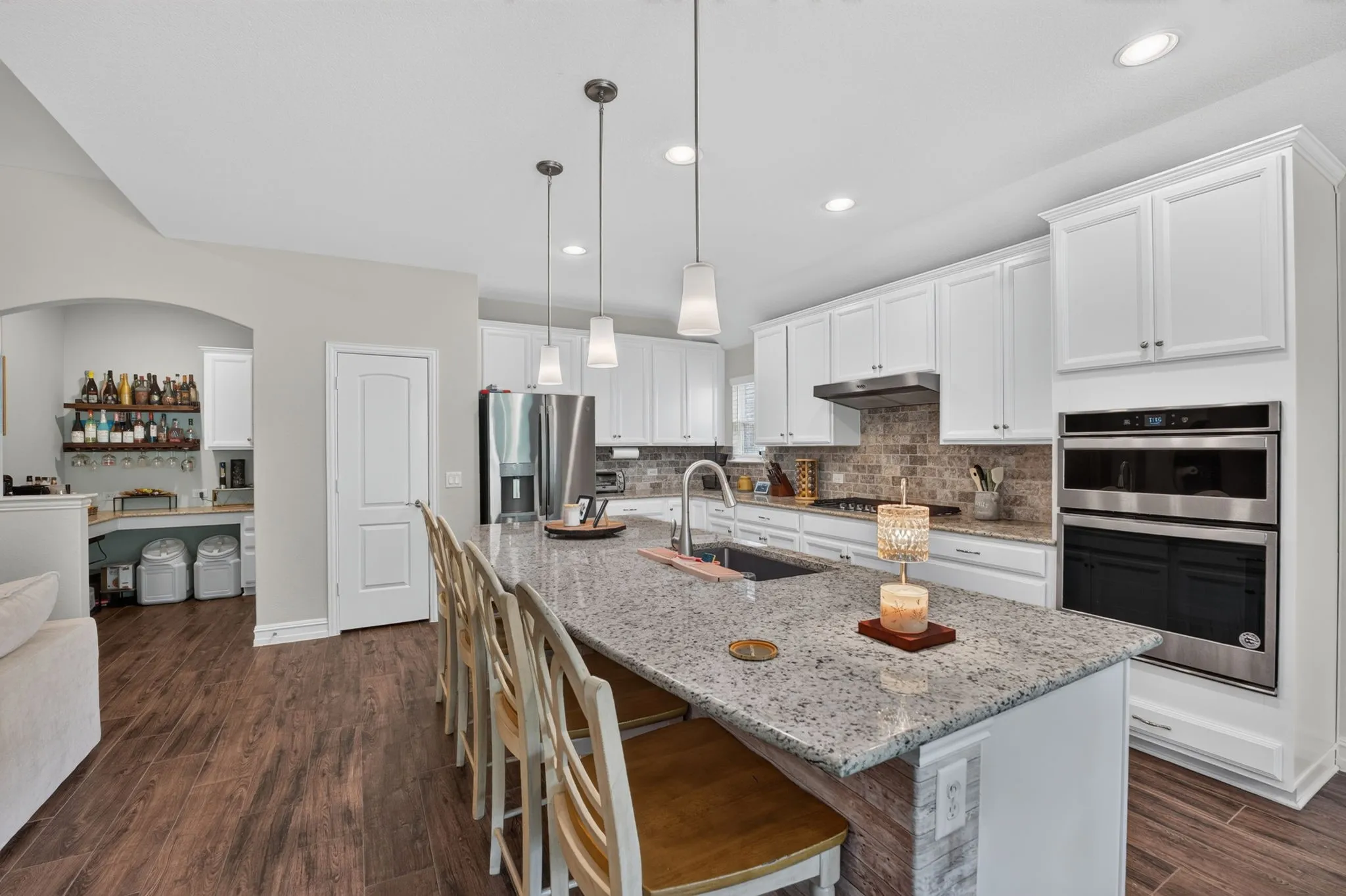 Gourmet kitchen featuring a large island with a stone countertop, white cabinetry, built-in stainless steel double ovens, and wood-finish flooring