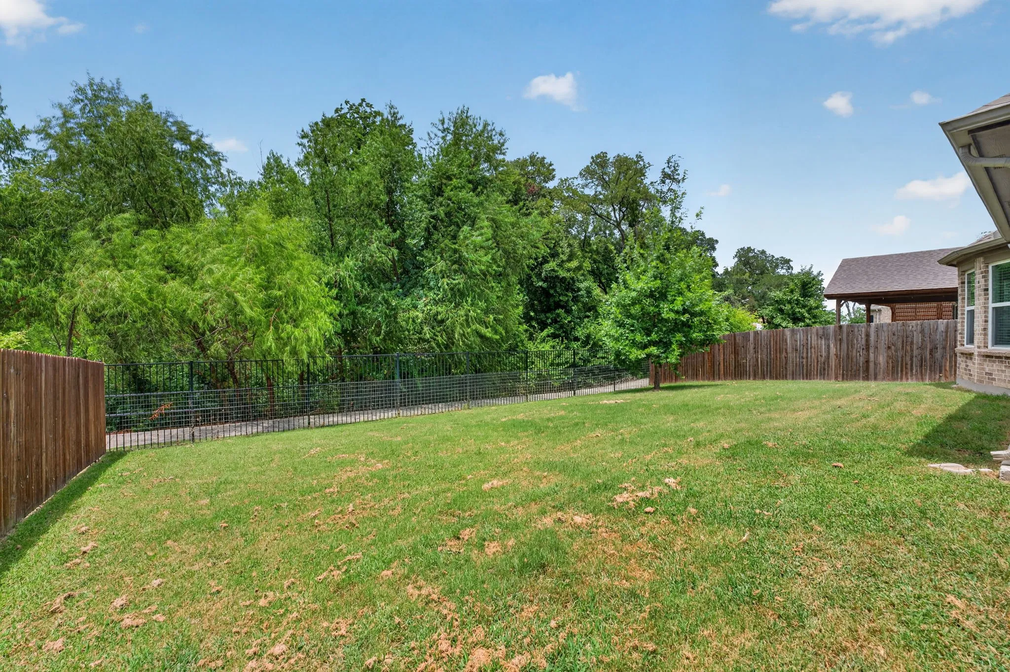 Expansive green lawn surrounded by mature trees, featuring a combination wood and wire fence