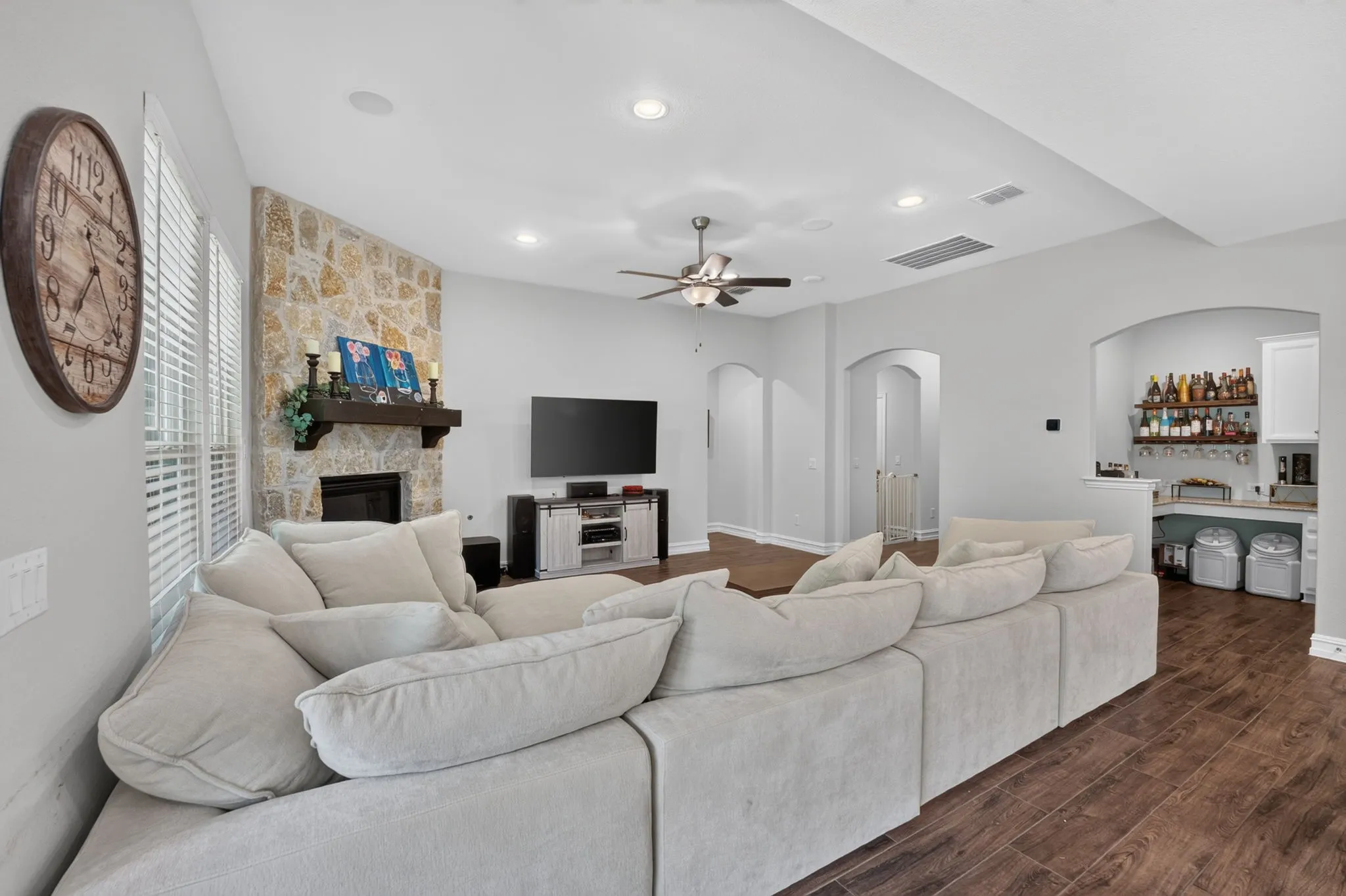 Spacious living area featuring a stone-clad fireplace with a dark wood mantle, wood-finish flooring, a ceiling fan, recessed lighting, and arched doorways