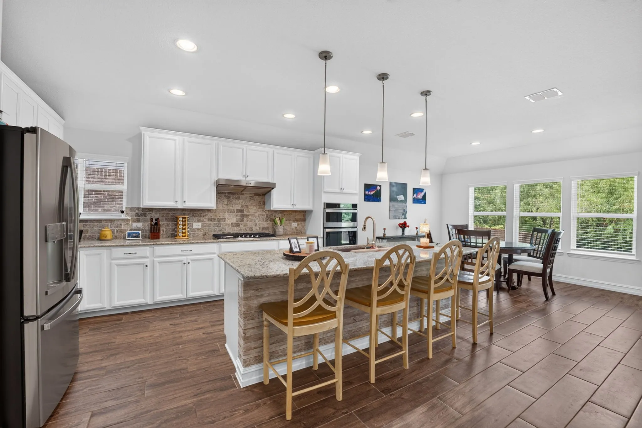 Spacious kitchen and dining area featuring an expansive island with seating, white cabinetry, integrated stainless steel appliances, and wood-finish flooring