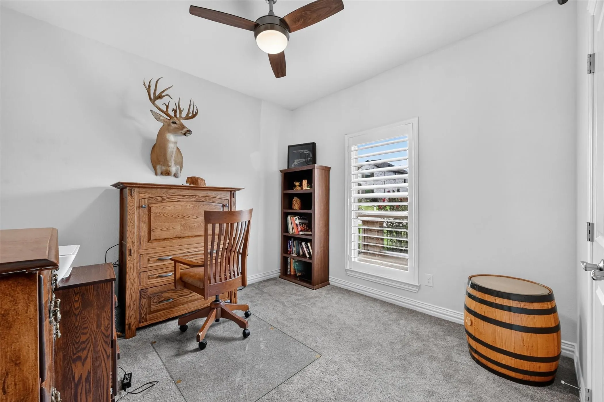 Carpeted room with a ceiling fan, white walls, and a window featuring plantation shutters