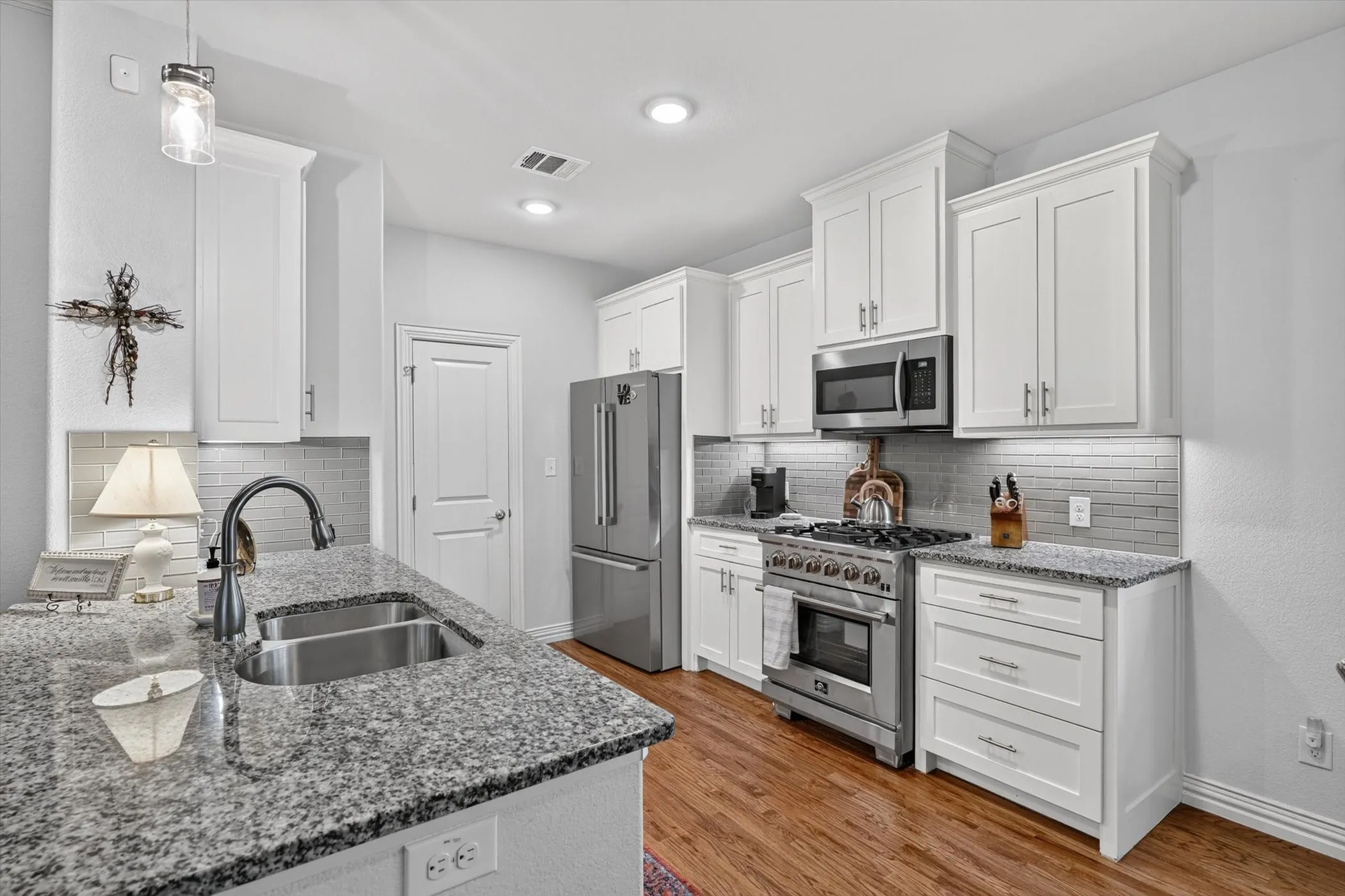Modern kitchen featuring white shaker cabinetry, stainless steel appliances, granite countertops, wood-finish flooring, and a subway tile backsplash