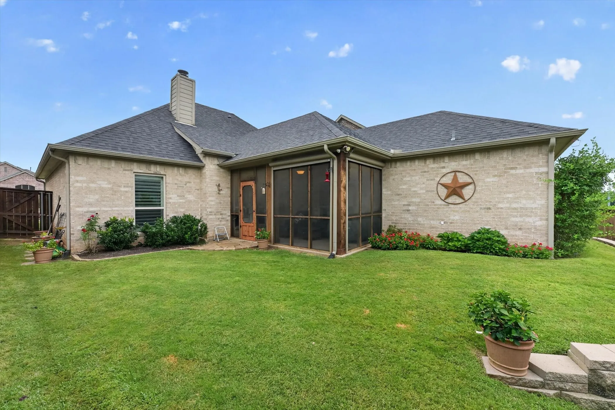 Expansive lawn area featuring a screened porch with a wood-finish door, light-colored brick exterior, and dark shingle roof