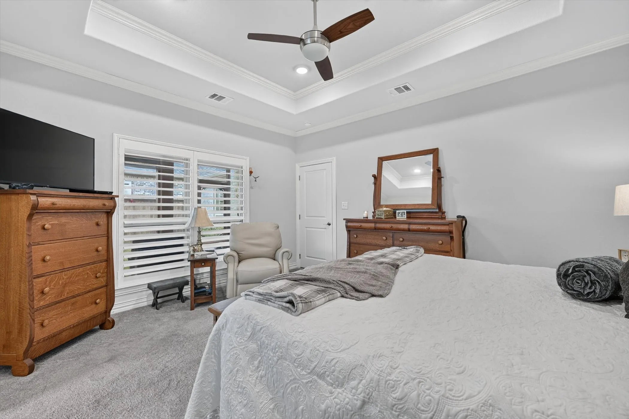 Tray ceiling with crown molding, ceiling fan, recessed lighting, carpet flooring, and window with plantation shutters
