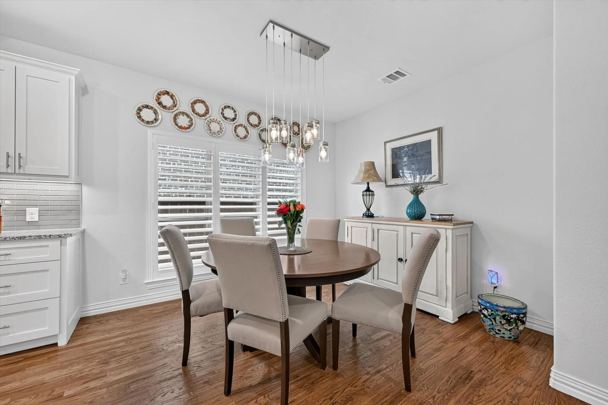 Dining area featuring wood-finish flooring, white plantation shutters, and a linear chandelier