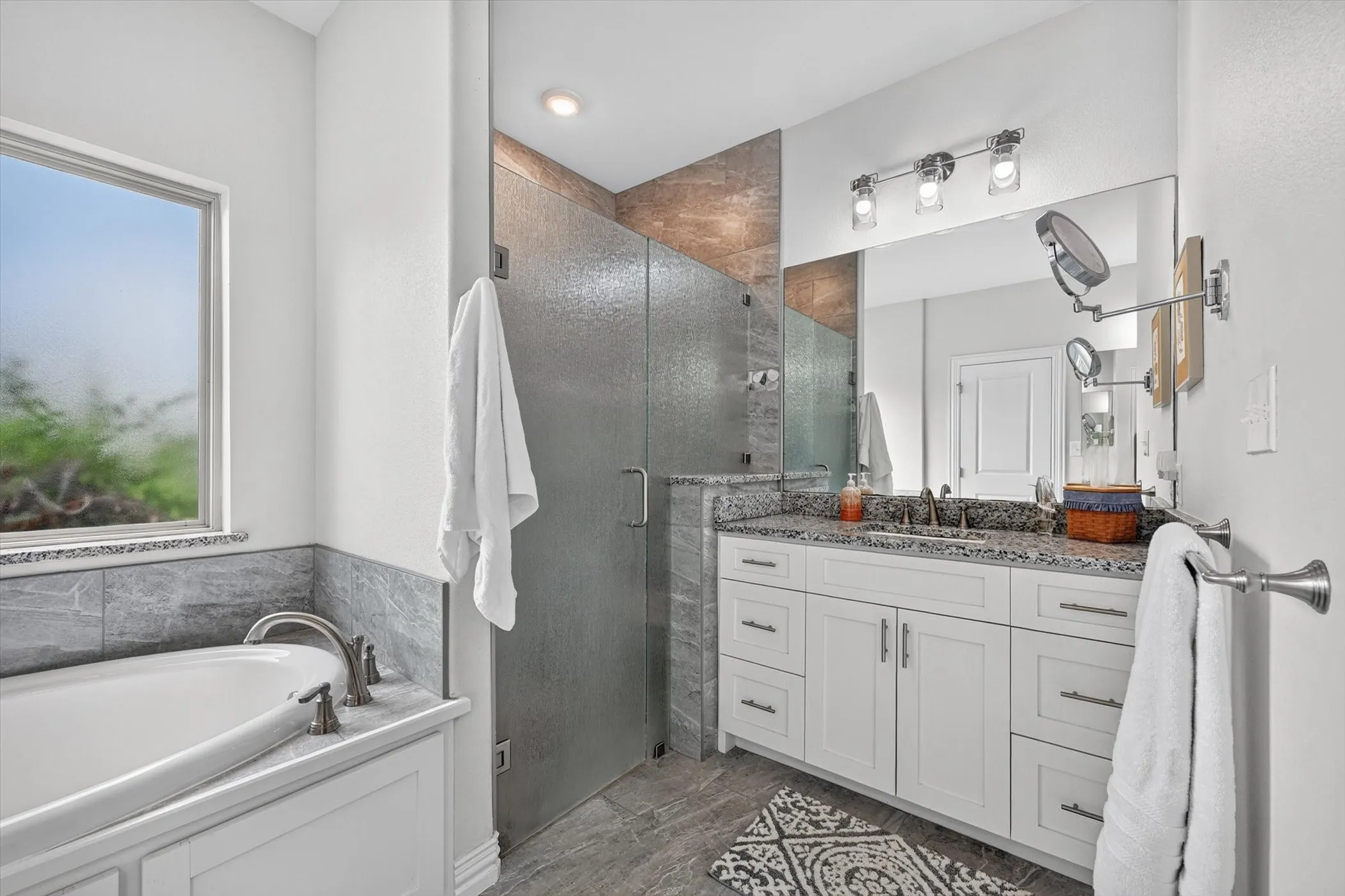 Contemporary bathroom featuring a freestanding tub, glass-enclosed shower, white vanity with stone countertop, and large mirror