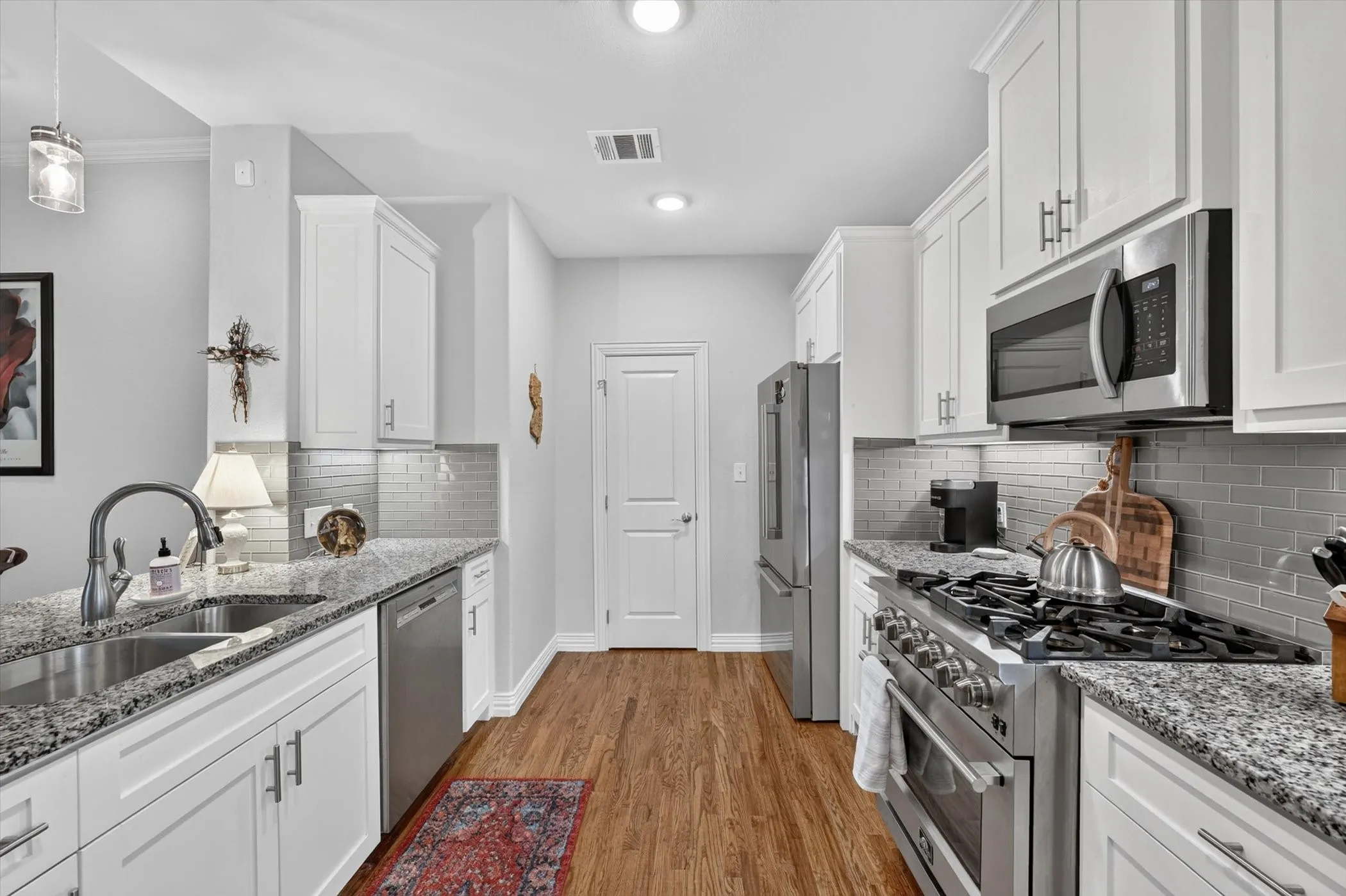 Well-appointed kitchen featuring granite countertops, stainless steel appliances, white cabinetry with contemporary hardware, a subway tile backsplash, and wood-finish flooring
