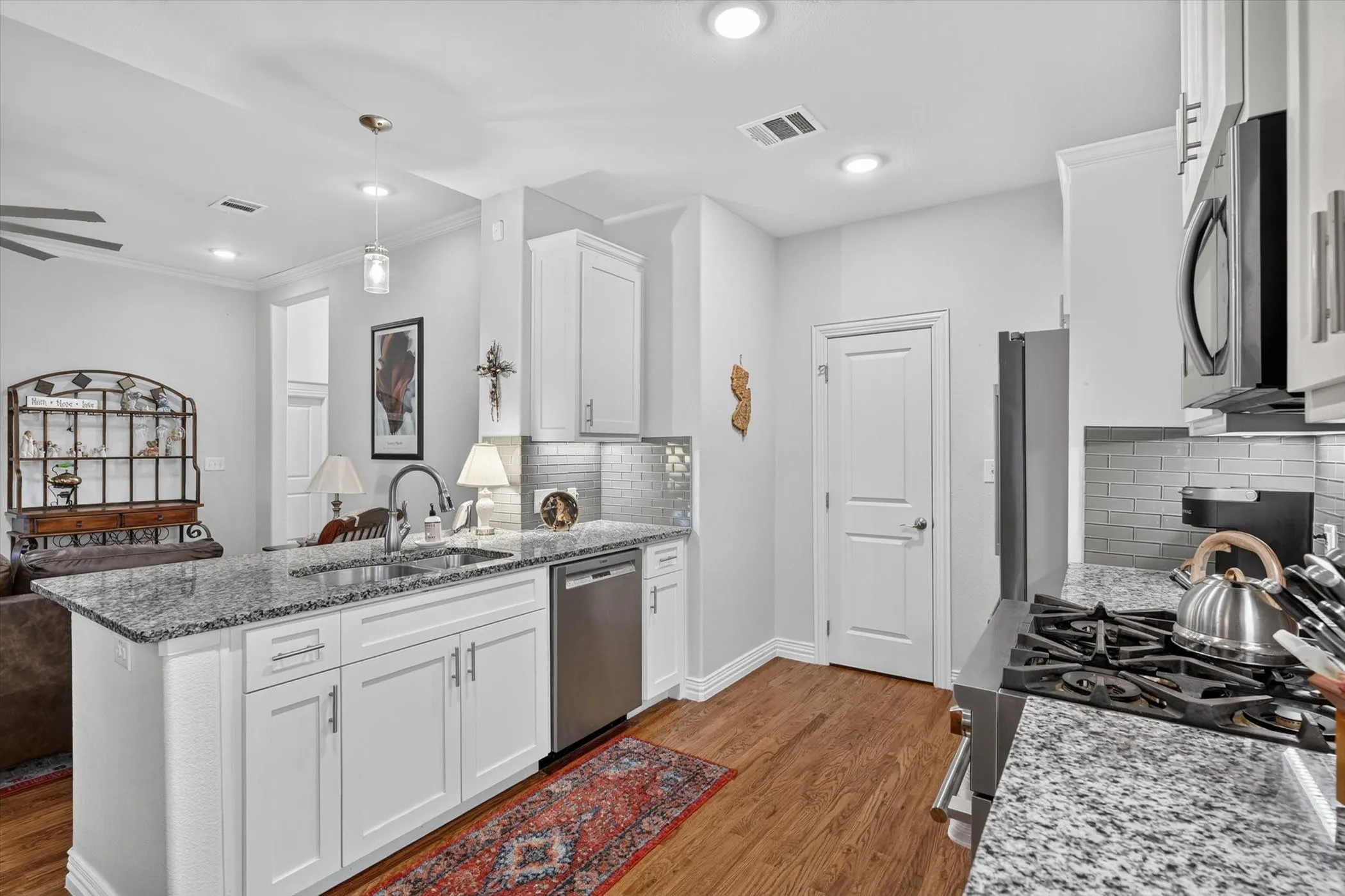 Modern kitchen featuring white cabinetry, granite countertops, stainless steel appliances, wood-finish flooring, and subway tile backsplash